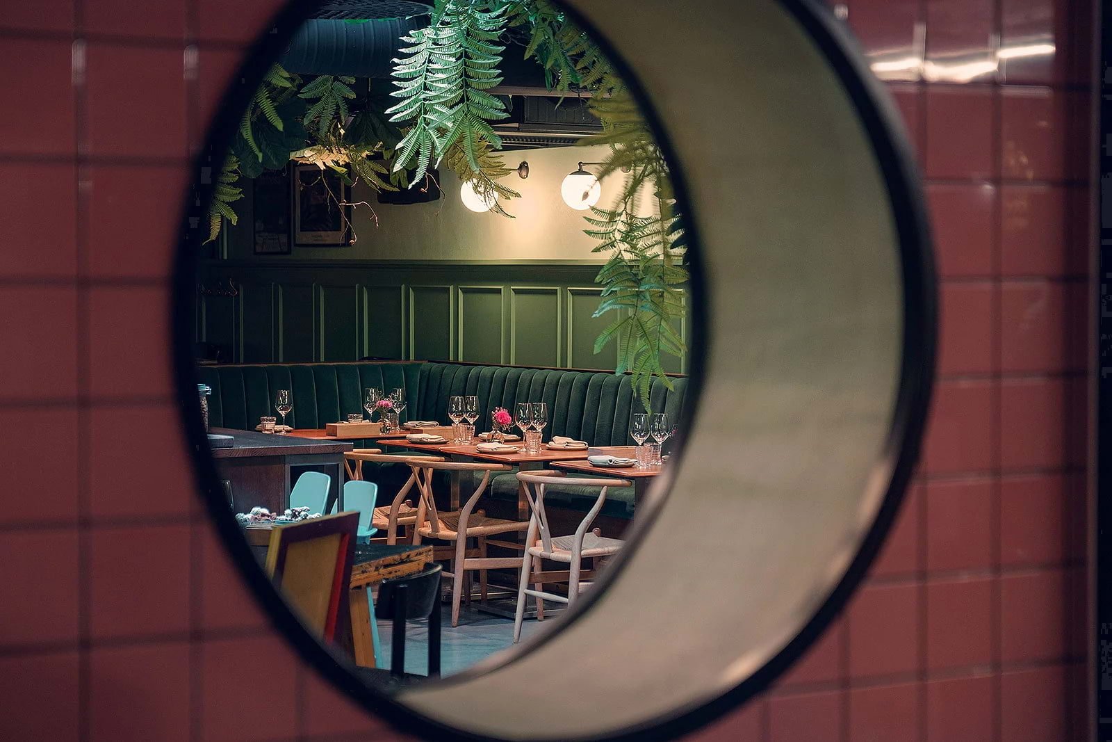 A green dining area with foliage, seen through a porthole in a pink tiled wall