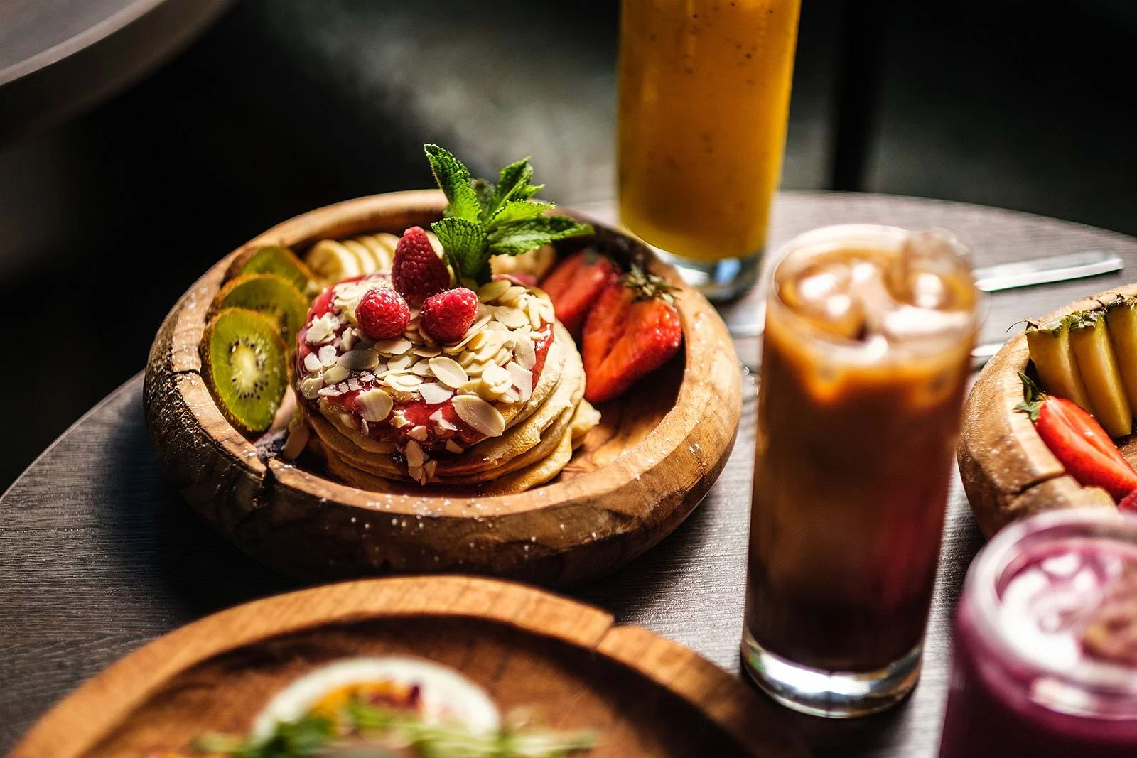 A stack of pancakes on a round wooden plate, covered with fruit and nuts