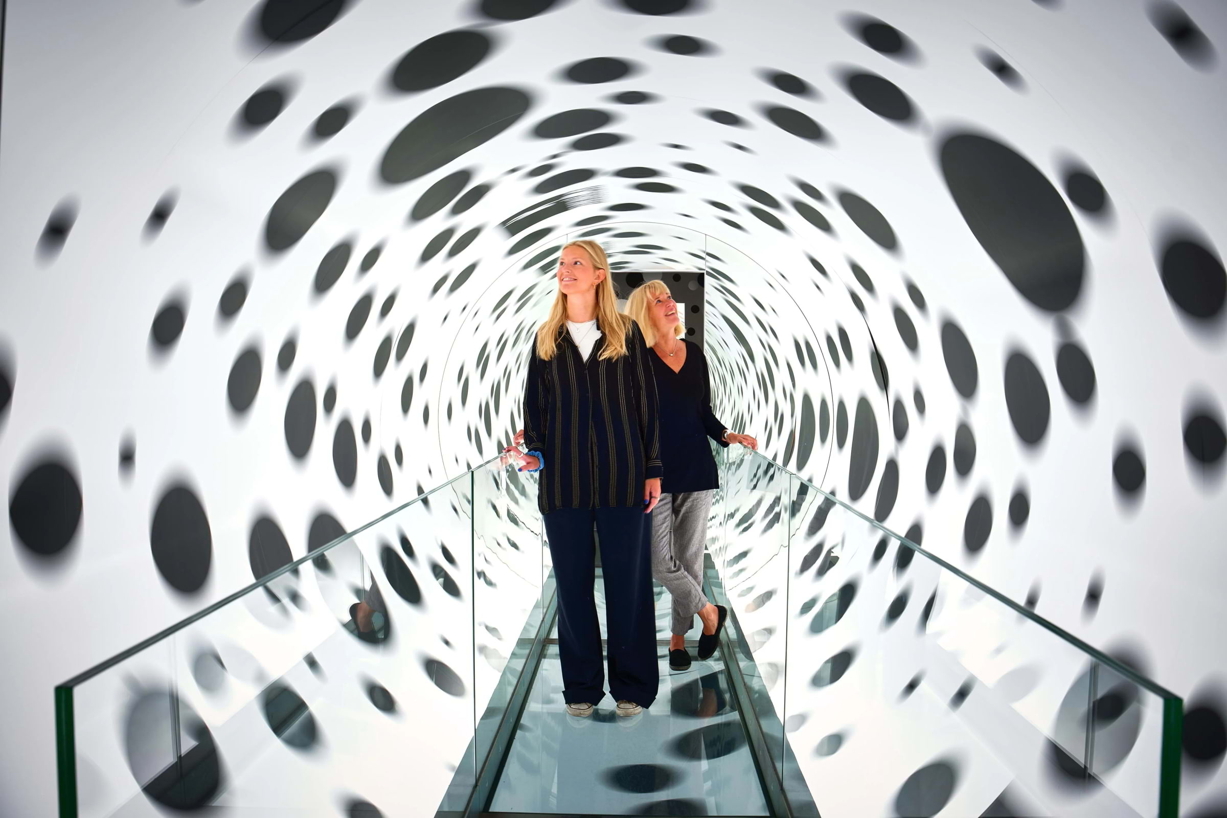 Two women walking through a trippy black-and-white tunnel