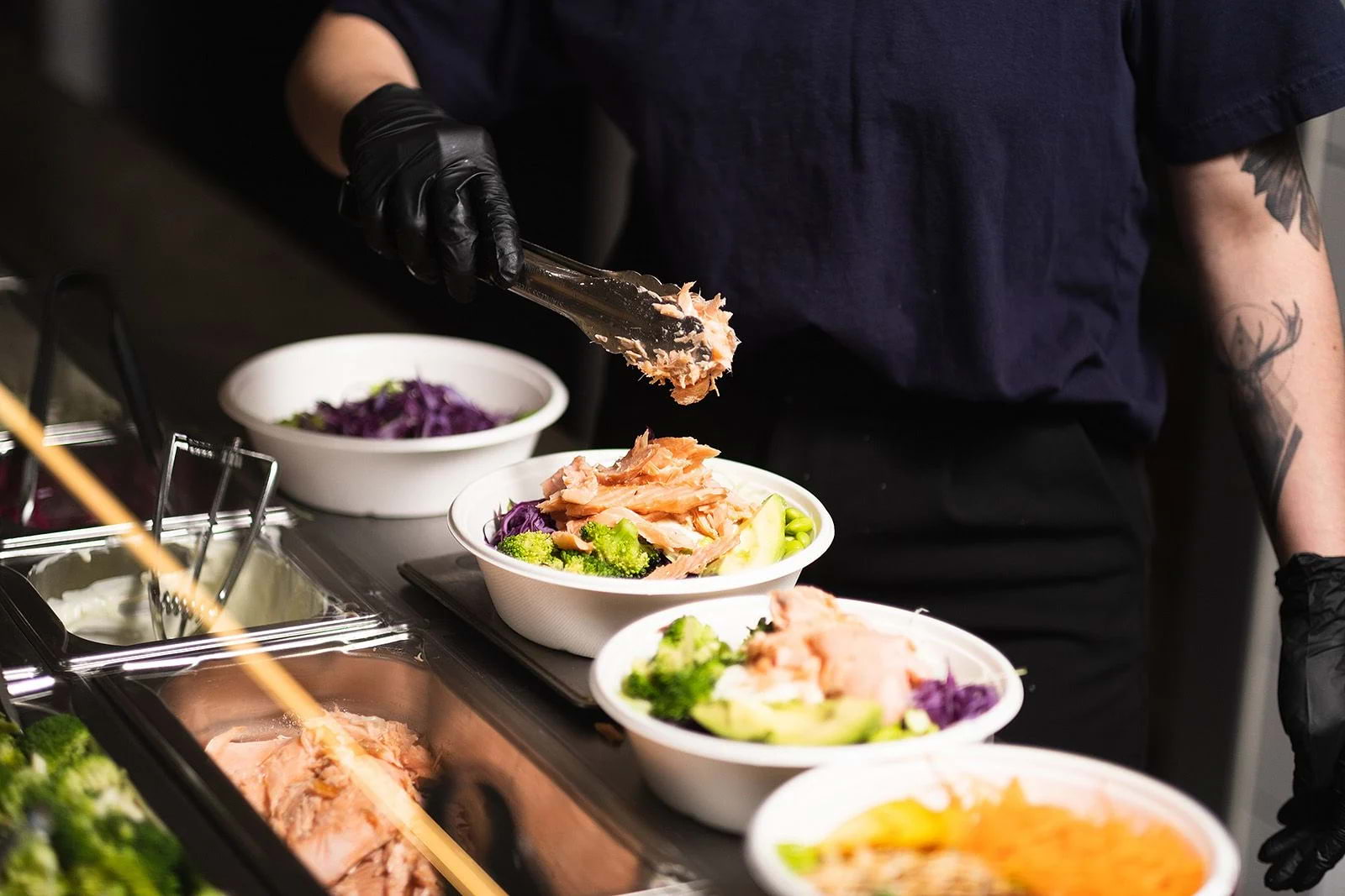 A server making four different salads at a salad bar