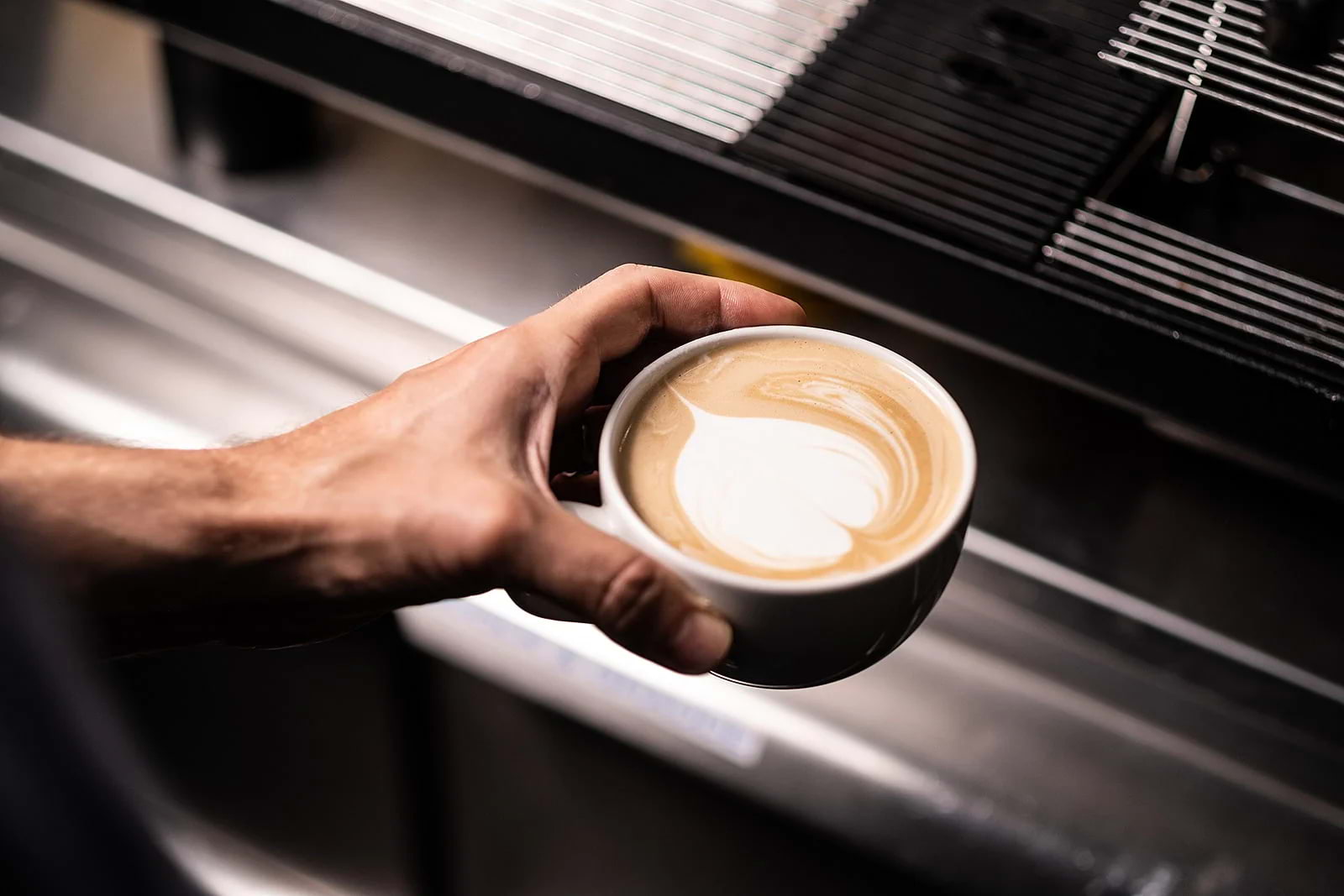 Close-up of a barista's hand holding a fresh cup of coffee