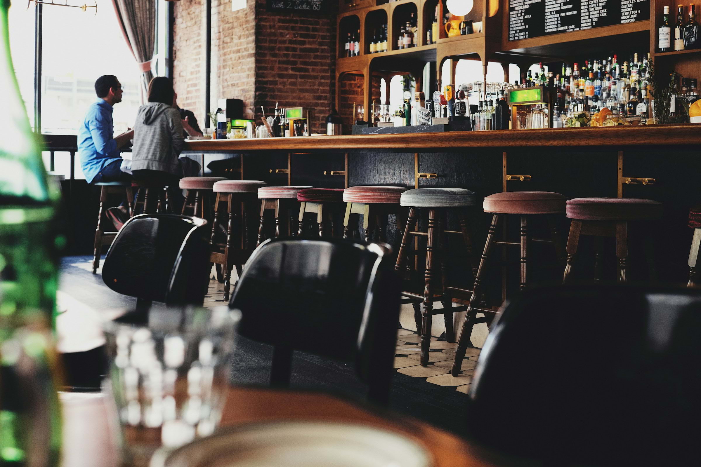 Two people sitting on bar stools in front of the bar in a pub