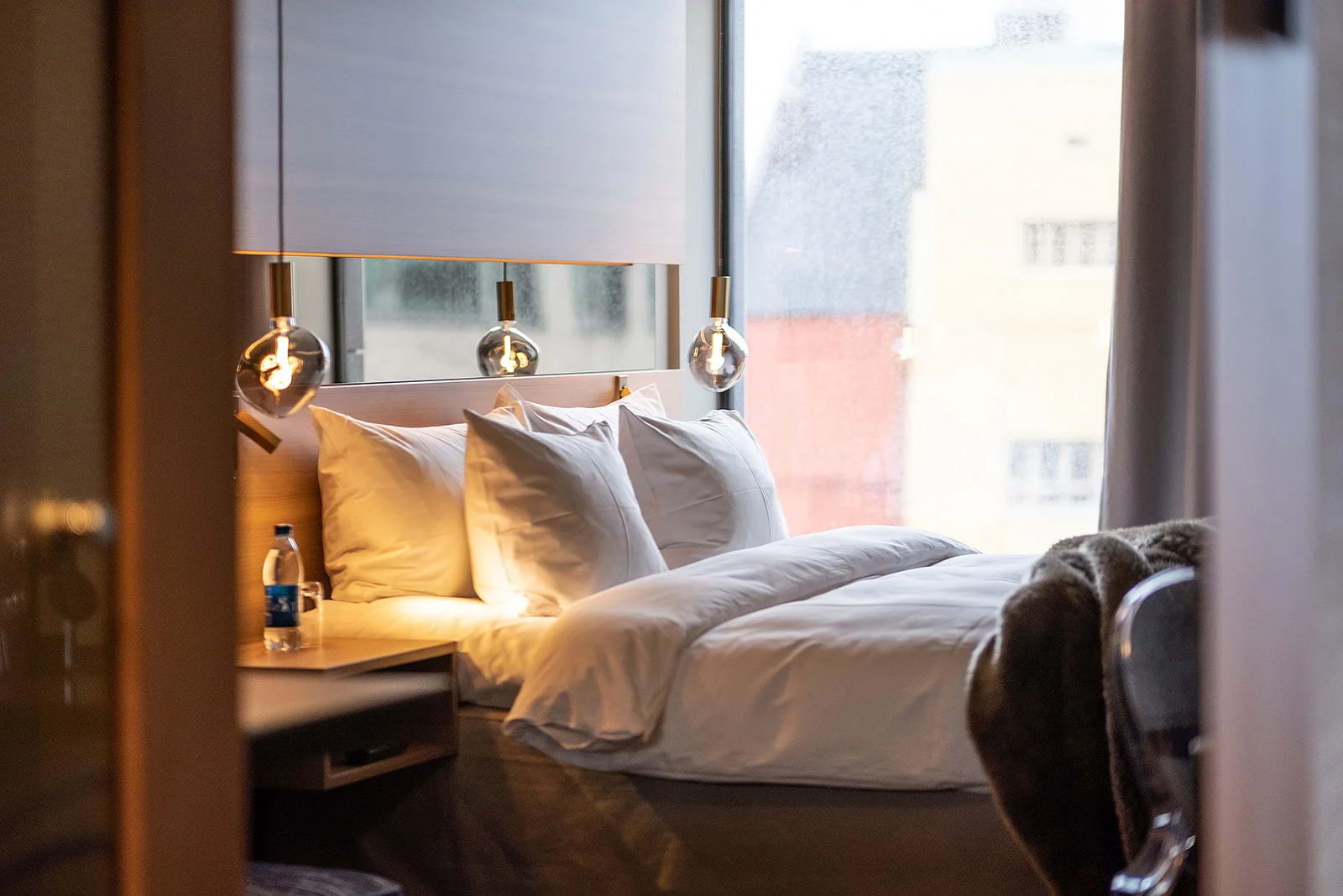 A double bed in a modern hotel room with a floor-to-ceiling window in the background