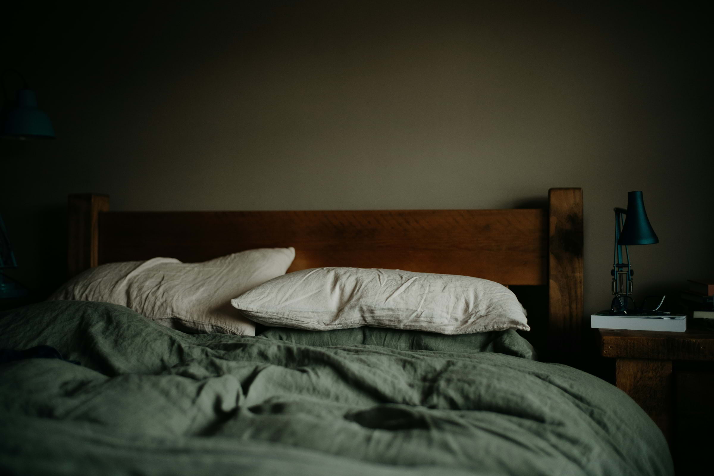 A cosy bed with a crumpled forest green duvet and pillows