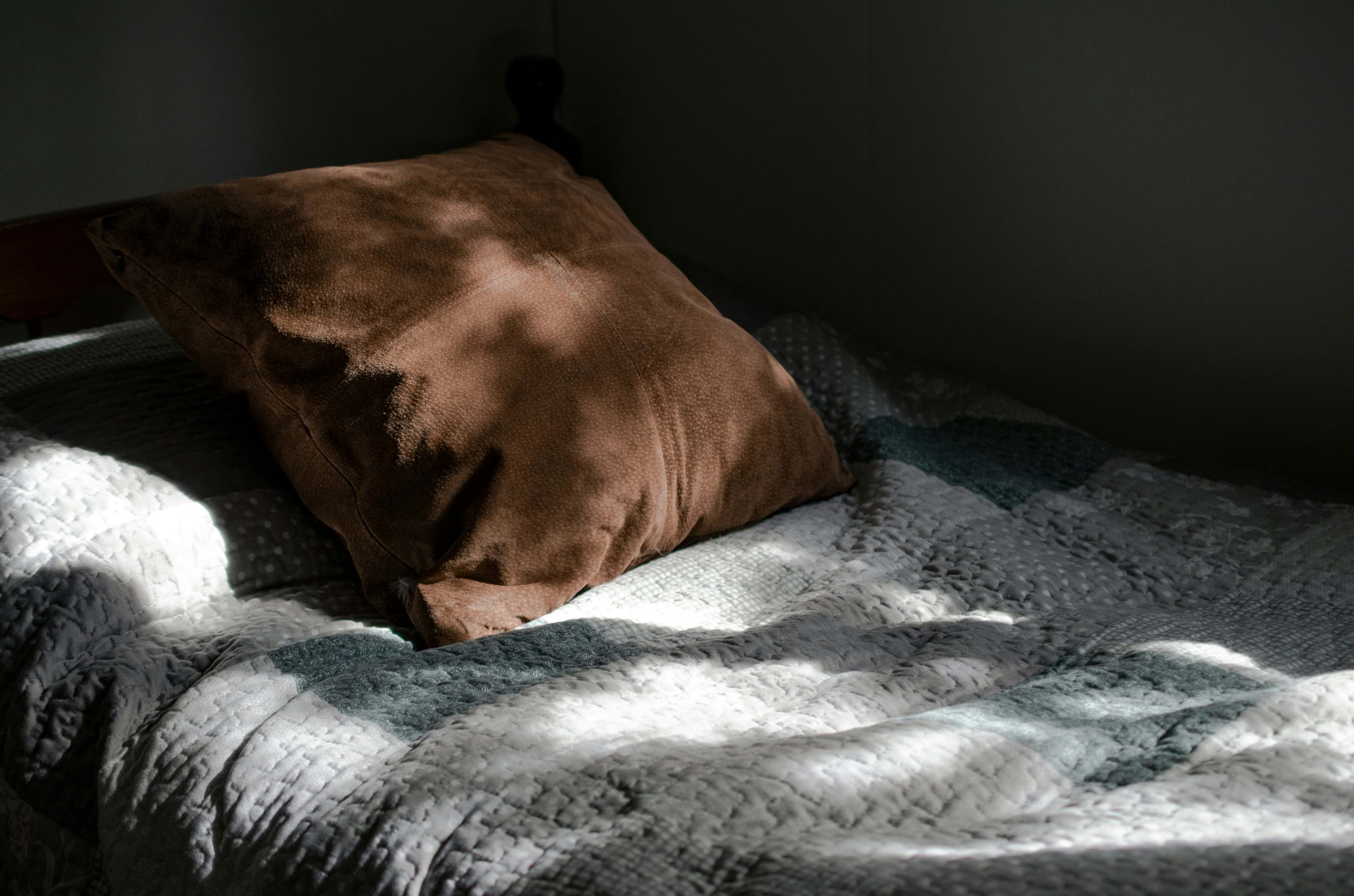 A crumpled duvet with a brown cushion with the mottled sun shining through