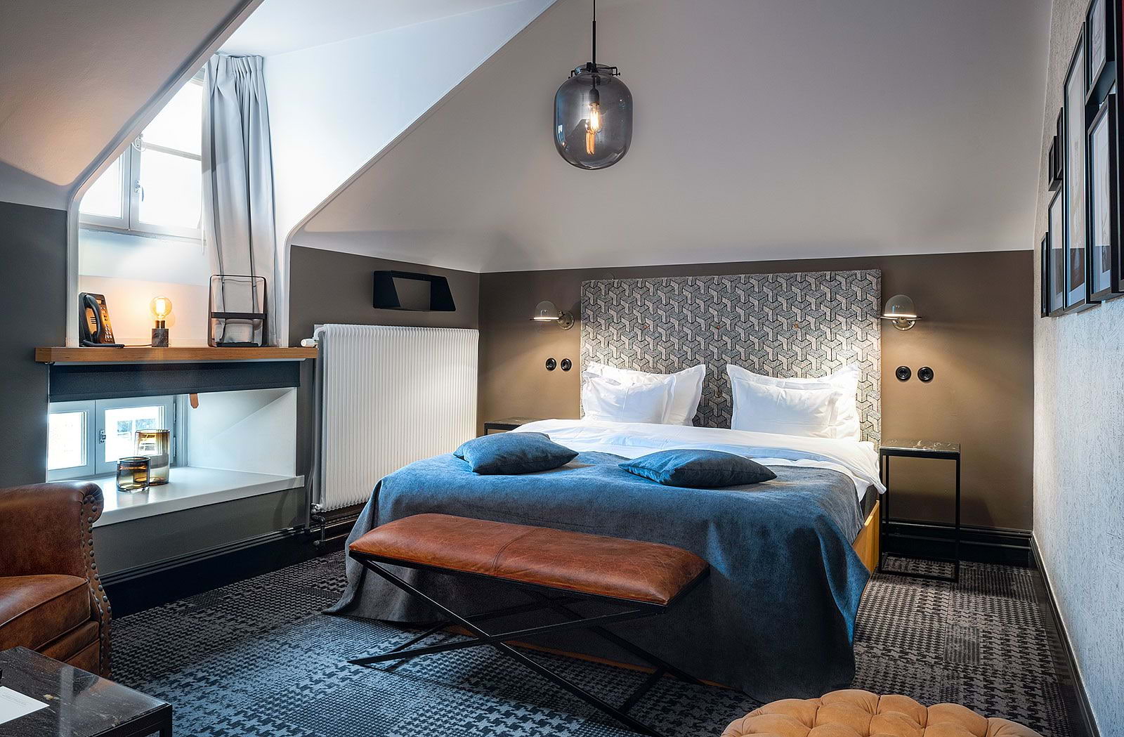 A stylish hotel room with a double bed, patterned carpeting, and a blue duvet