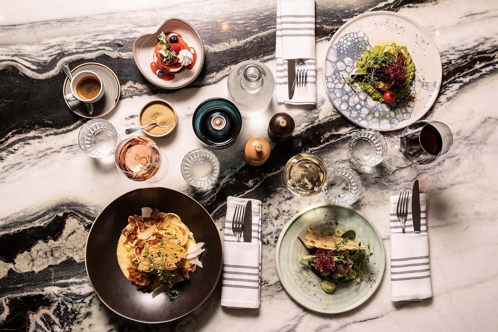 A bird's-eye view of an assortment of Italian dishes and drinks on a marbled restaurant table