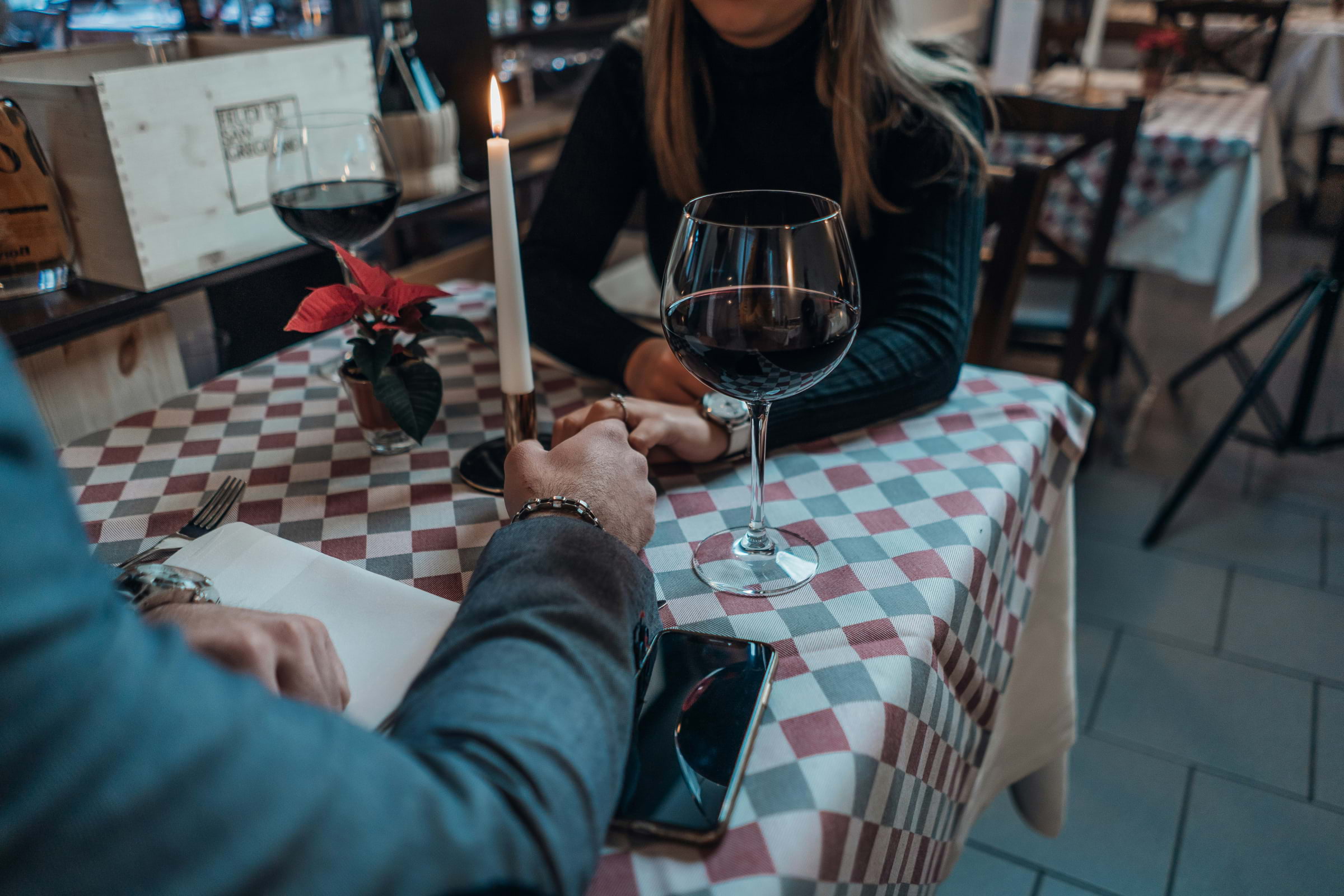 A table with a white candle, red wine and two people holding hands