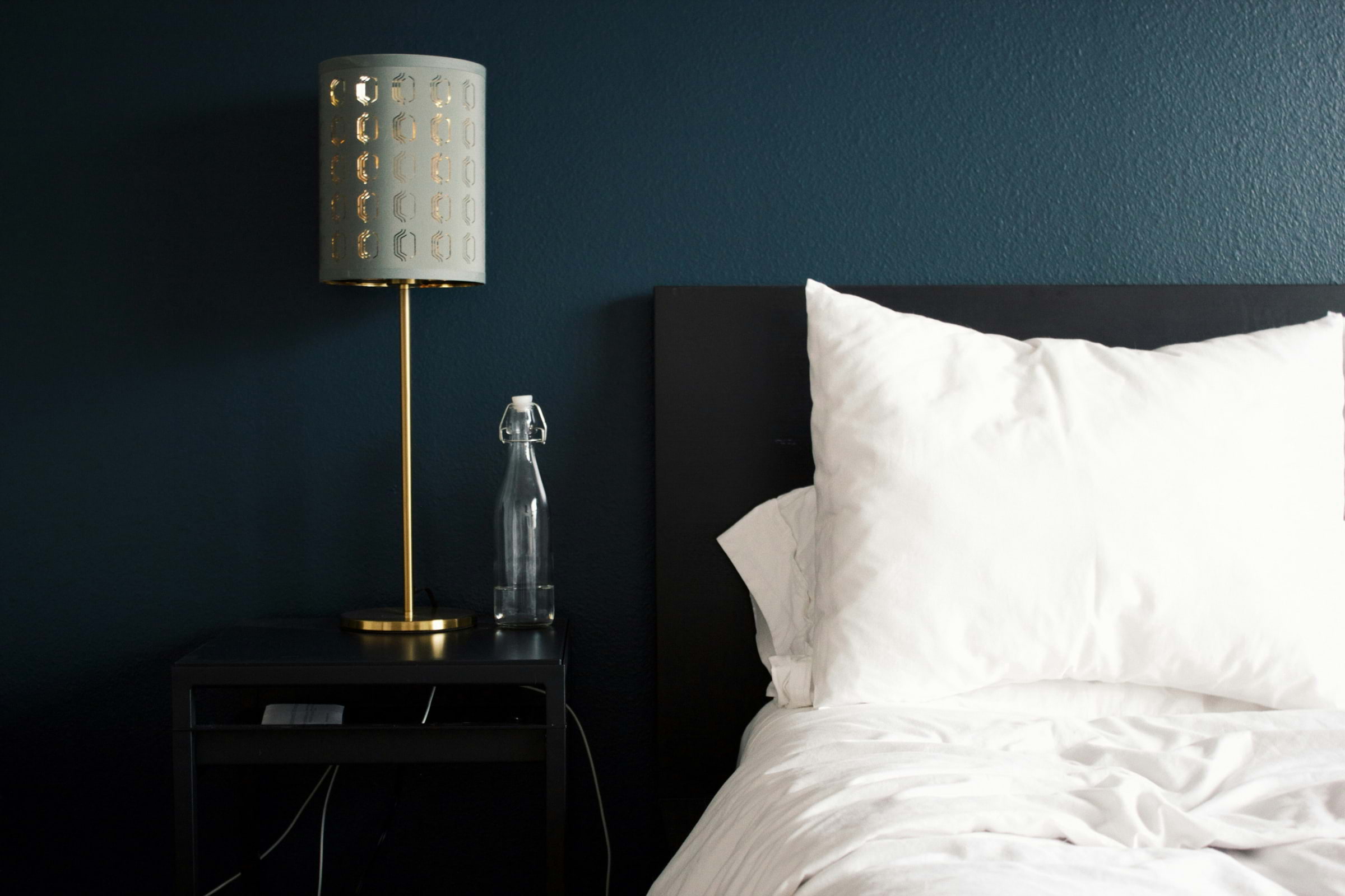 A bed against a navy wall with a lamp and sculpture next to it