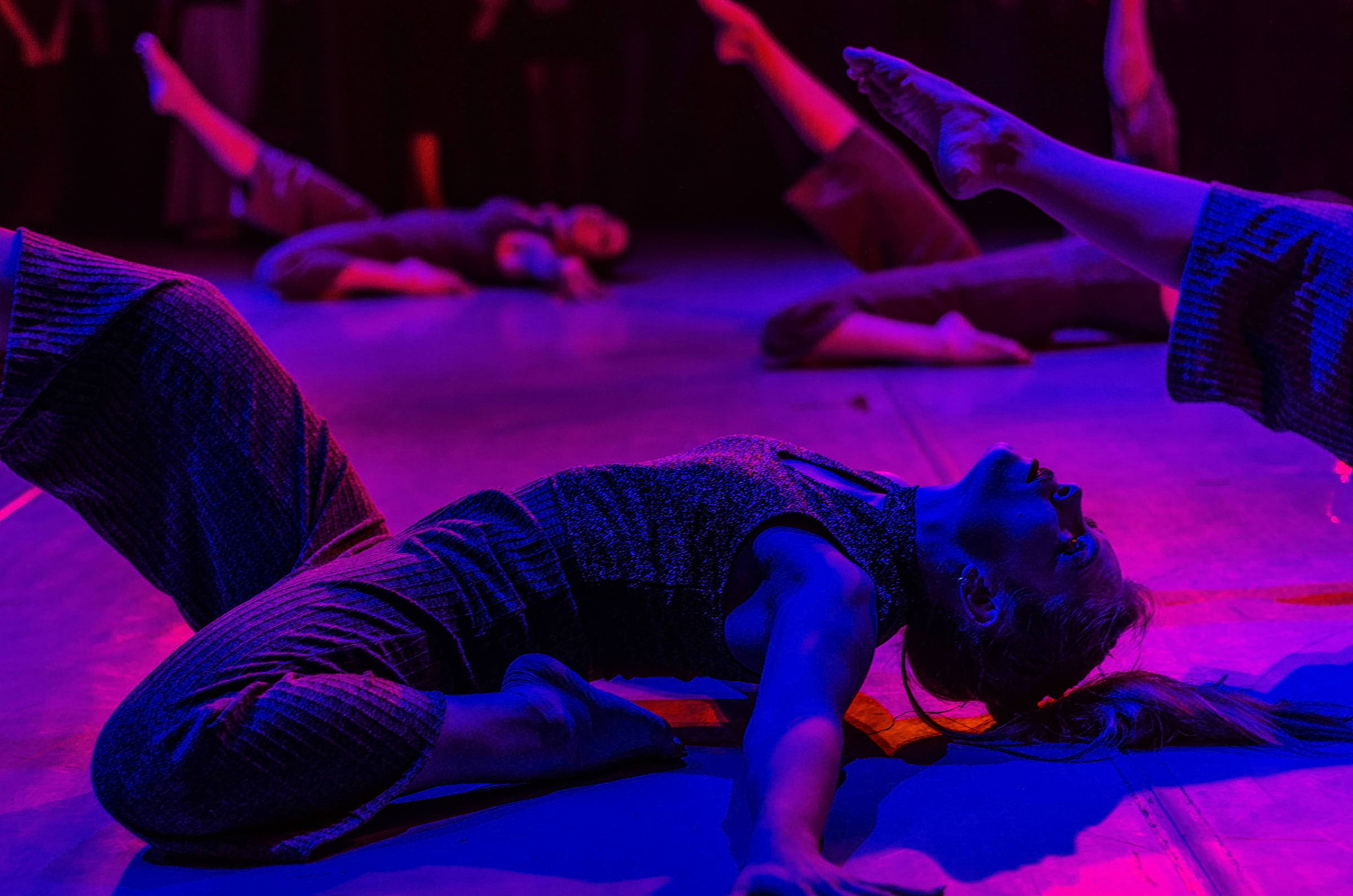 A woman doing a contemporary dance move in a dark, purple-lit room