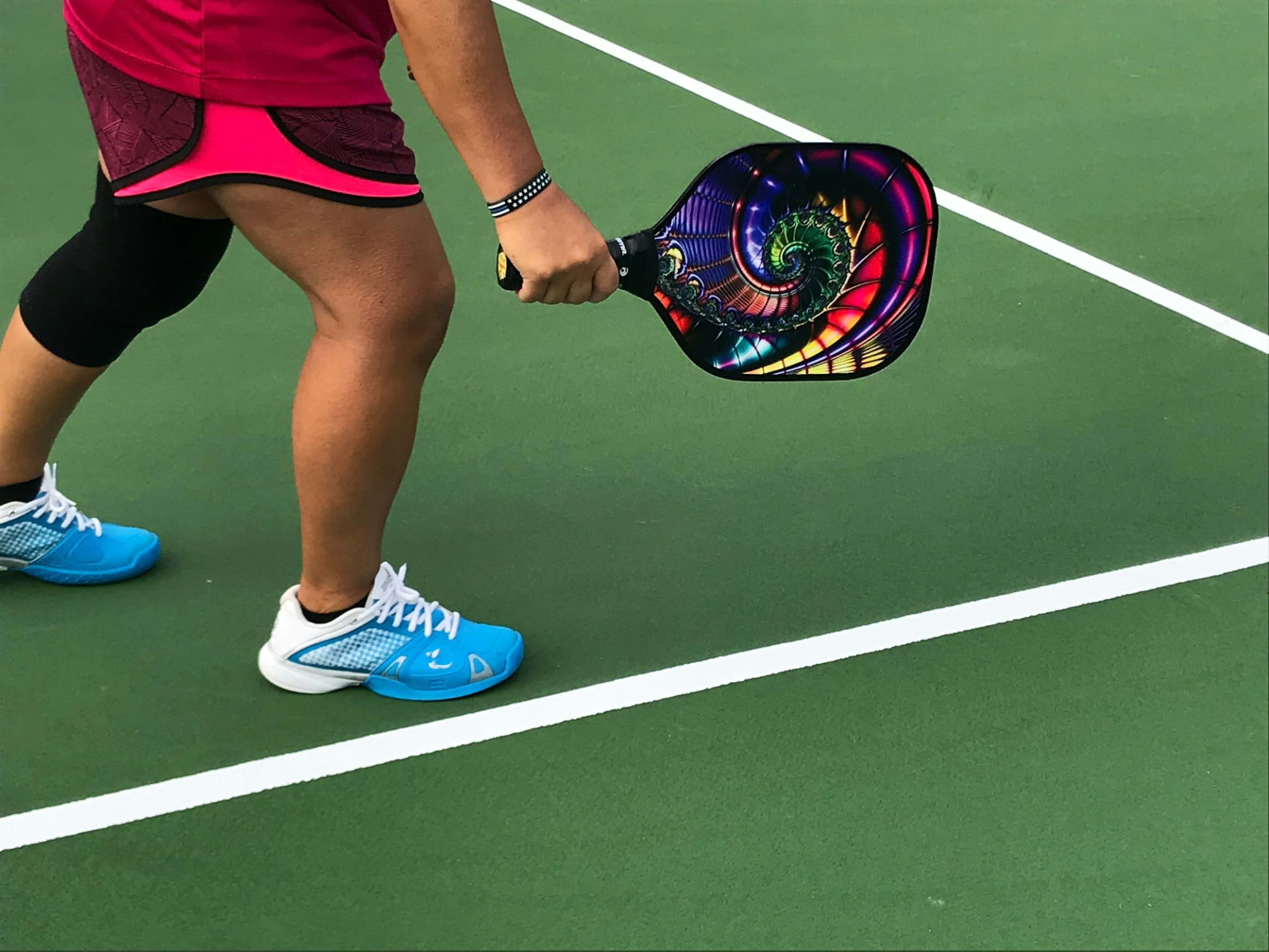 A player holding a colourful pickleball racket on a green court