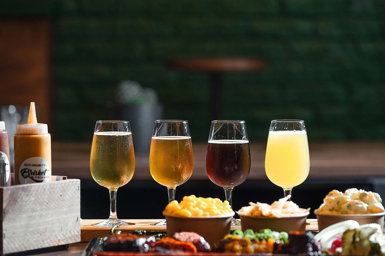 Four different beers lined up for a tasting, with small dishes around them