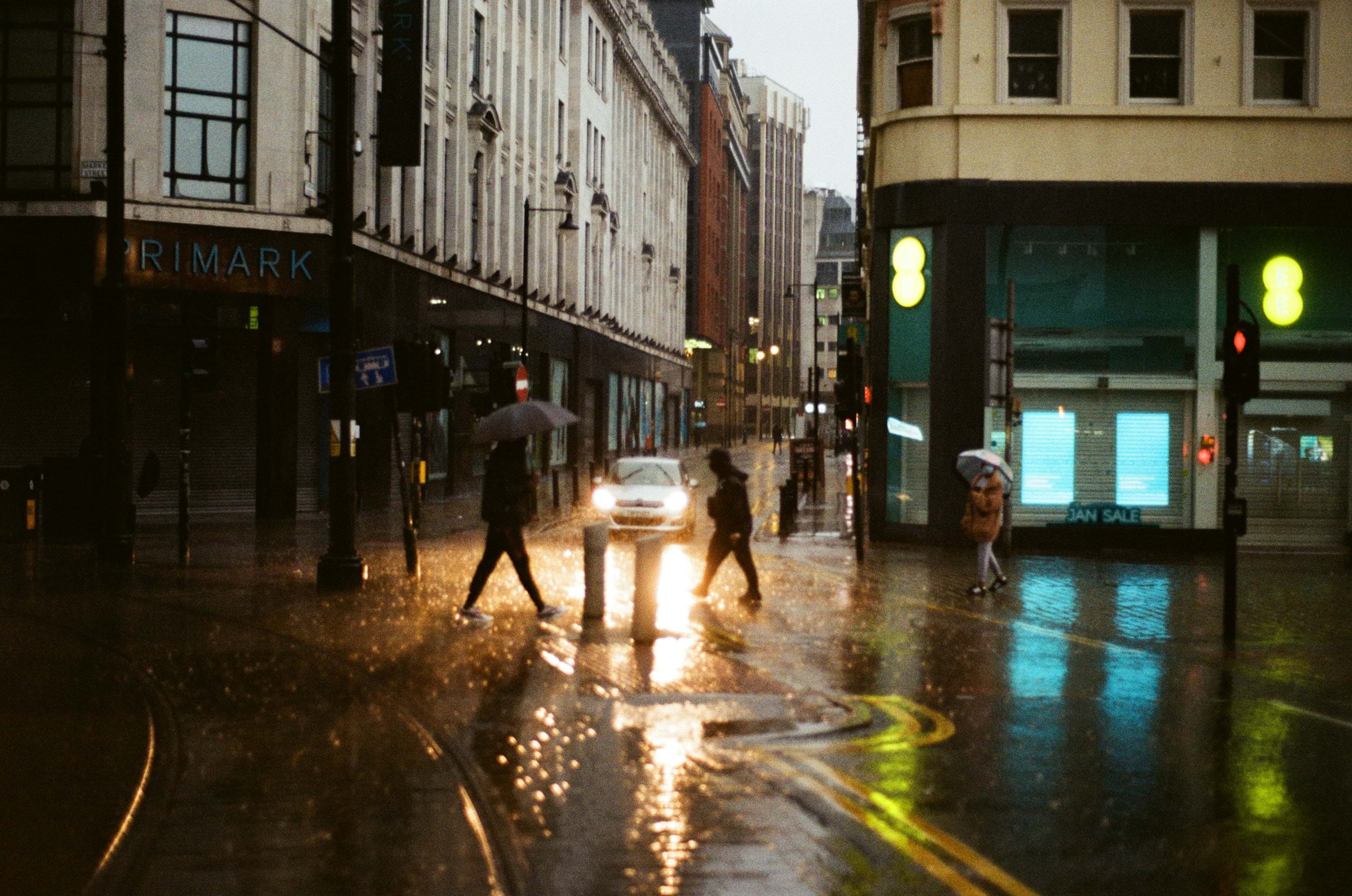 People with umbrellas walking across a Manchester street in the rain