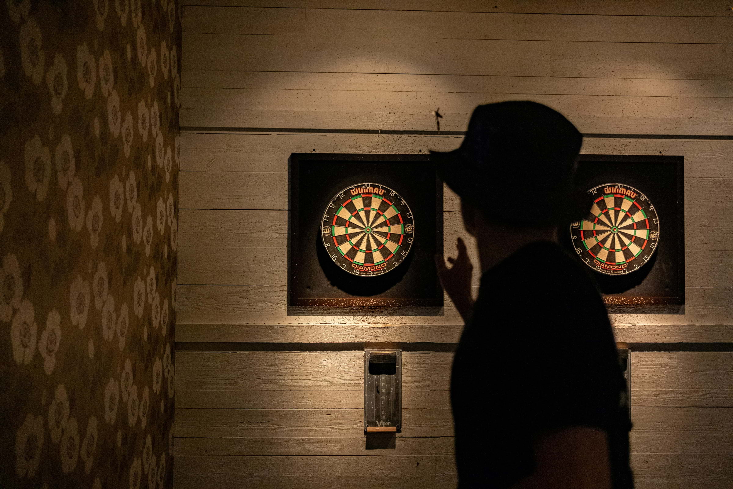 Silhouette of a person throwing a dart at a dartboard on a wooden wall