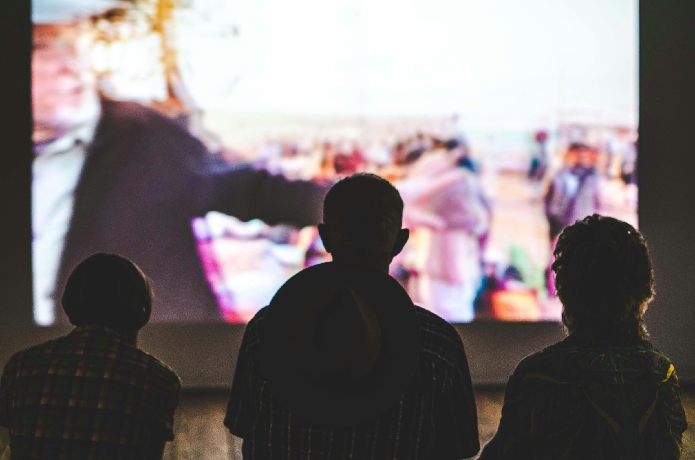 Silhouettes of three people watching a cinema screen