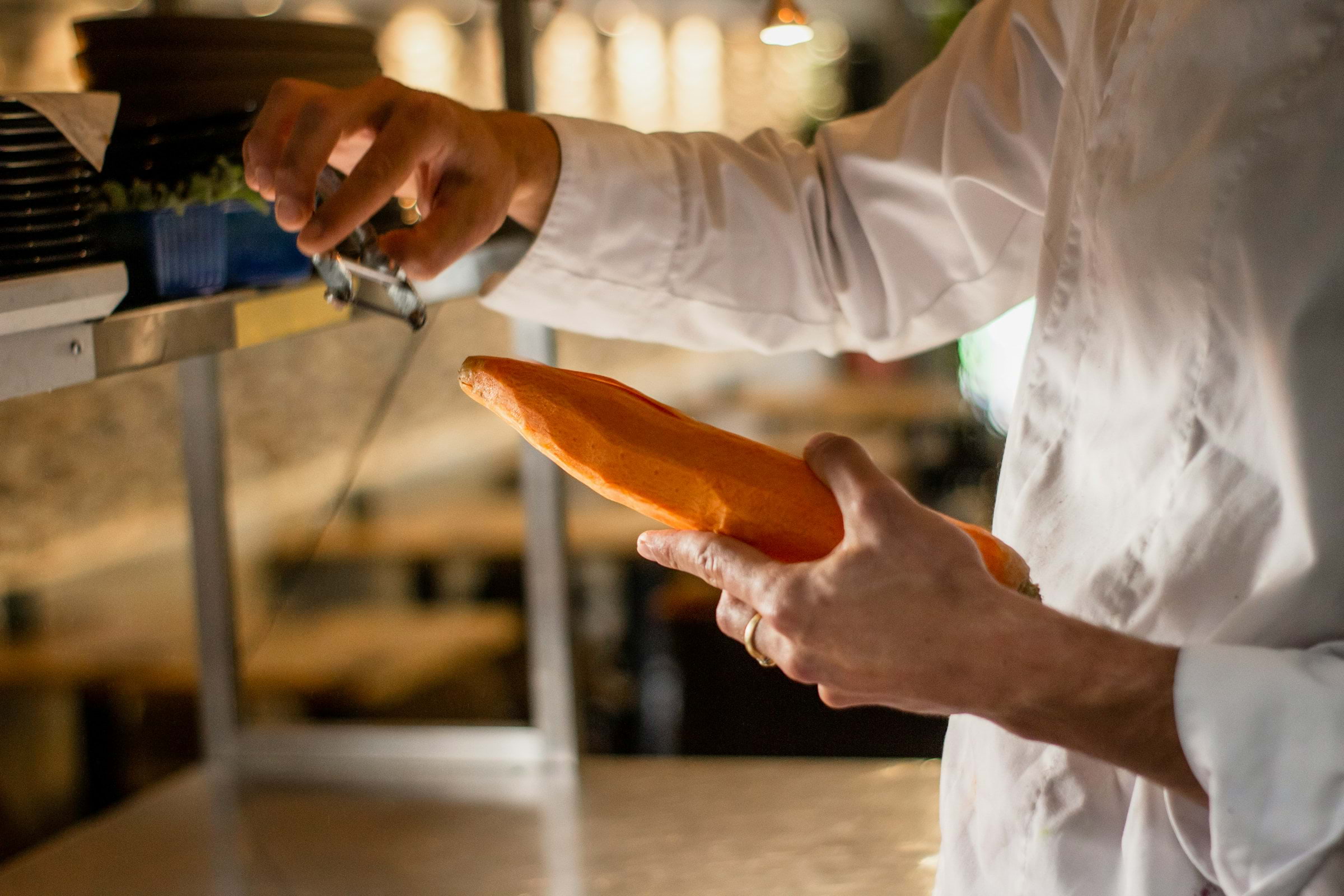 A close-up of a chef peeling a carrot in a restaurant kitchen