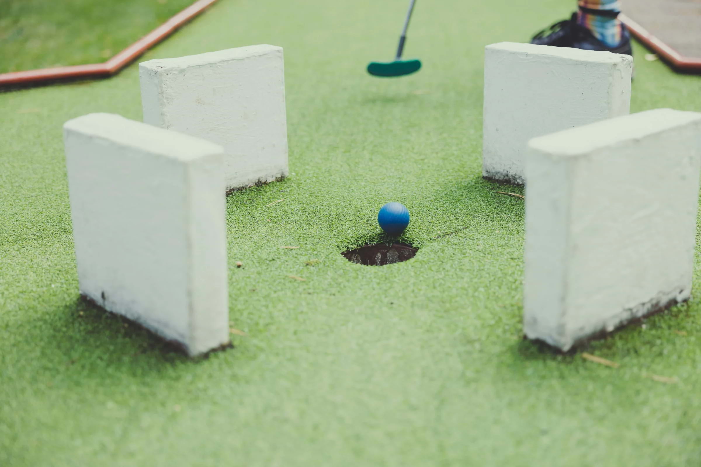 A golf ball moving into a hole on a mini-golf course
