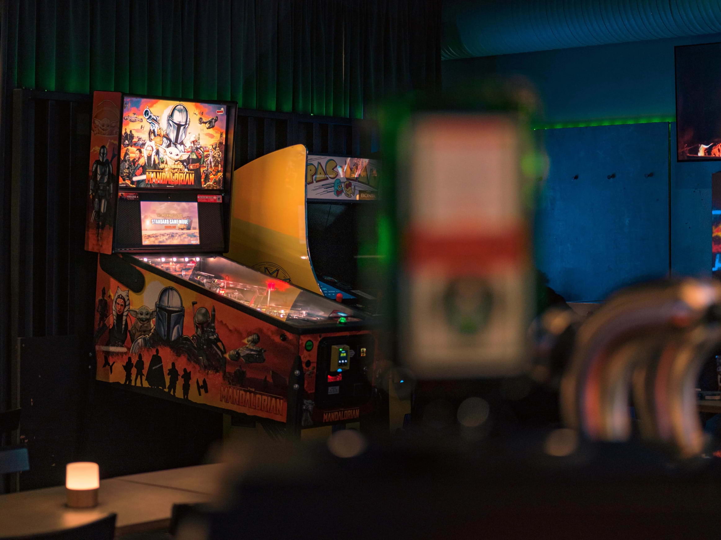 A pair of arcade machines lit up behind an out-of-focus bar