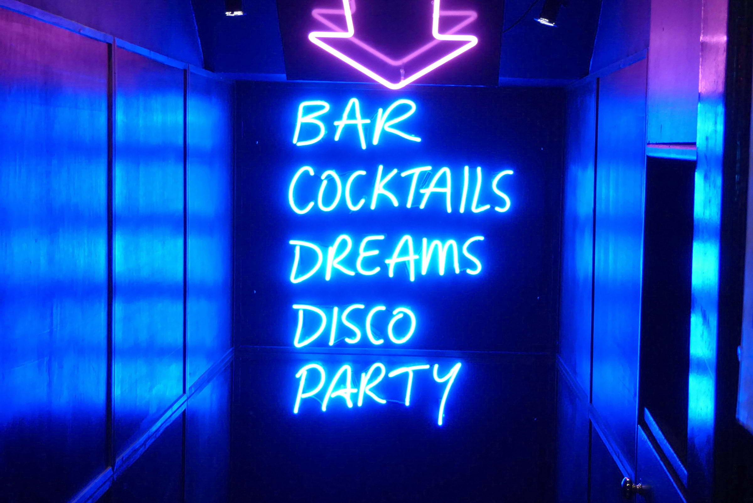 A neon sign pointing downstairs in a bar