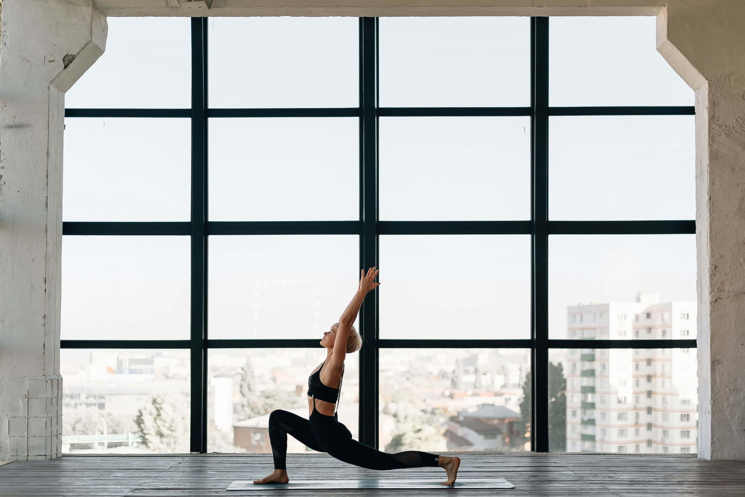 A woman in a yoga pose in front of a large window
