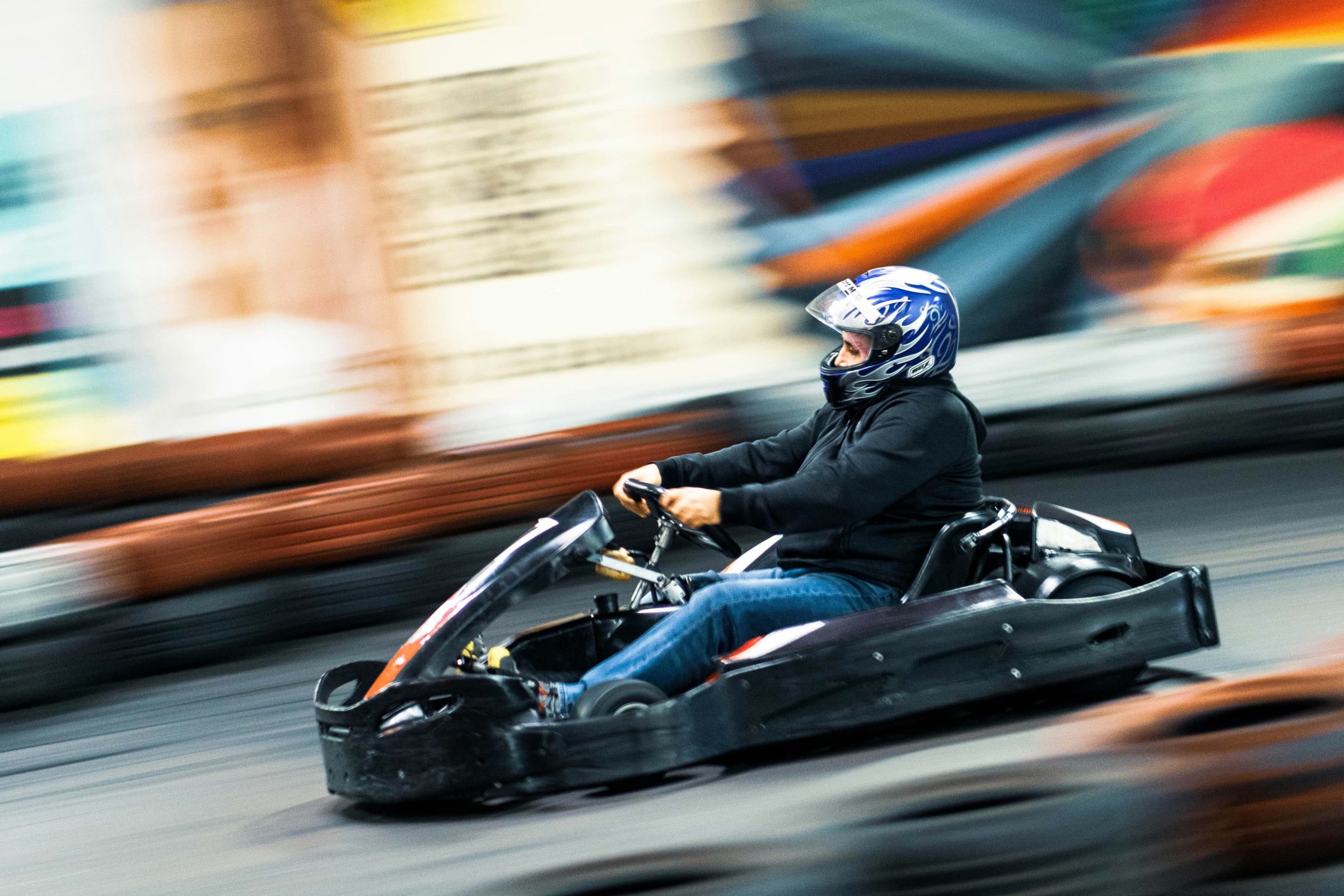 A driver in a black go-kart speeding along a go-karting track