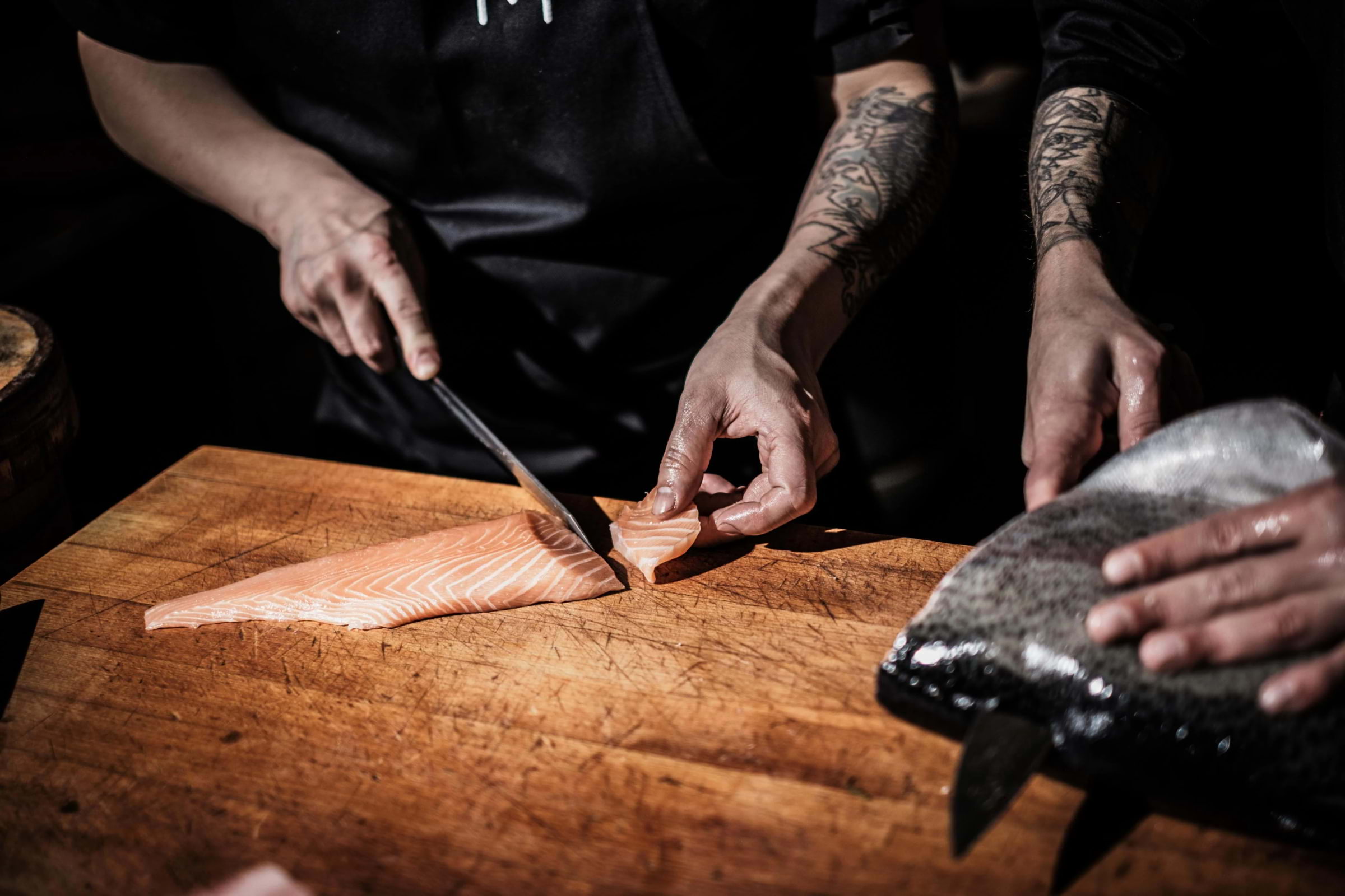 A close-up of two chefs in restaurant preparing fish for sushi on a wooden board