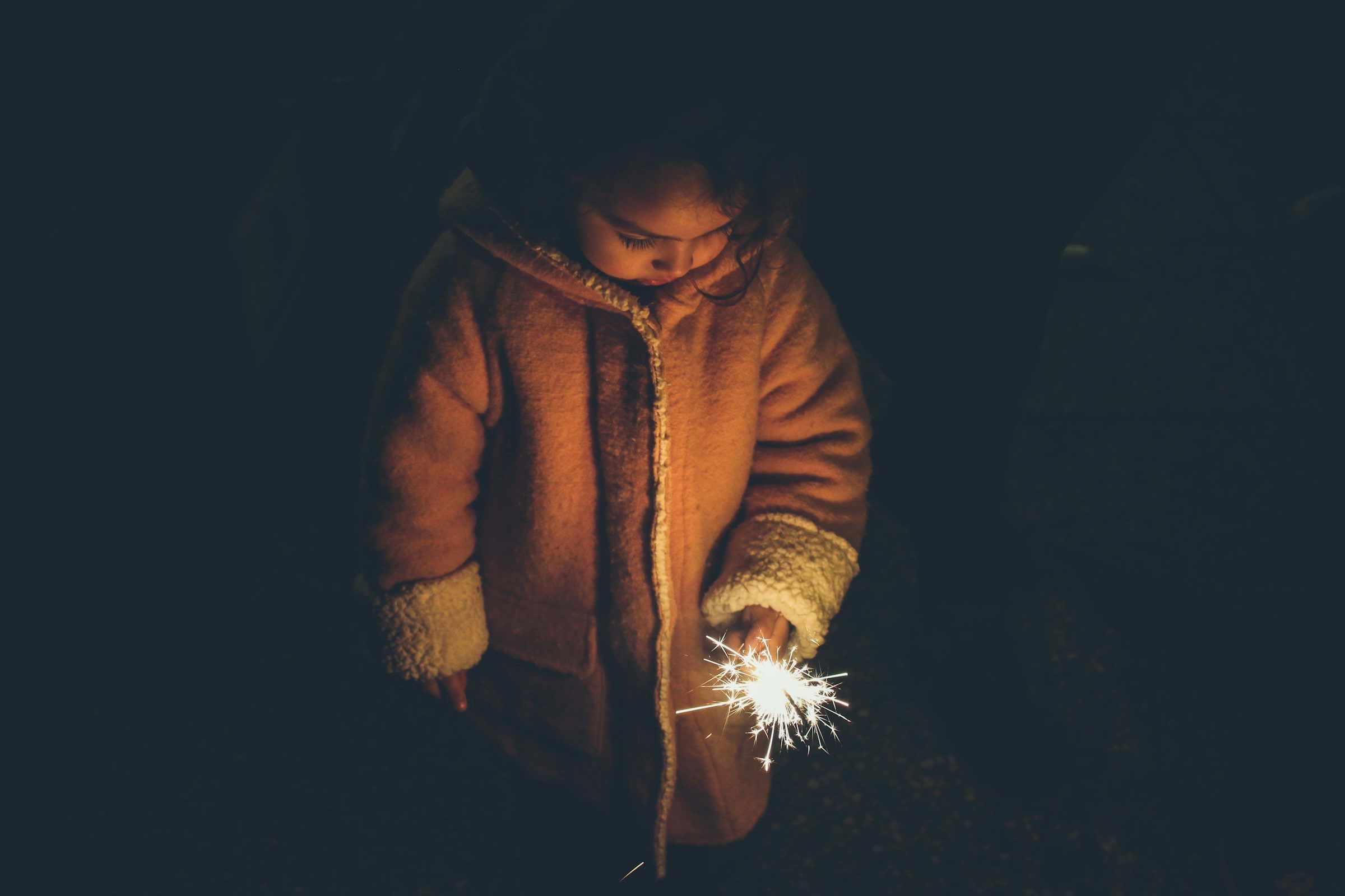 Girl in a winter coat holding a lit sparkler in the dark