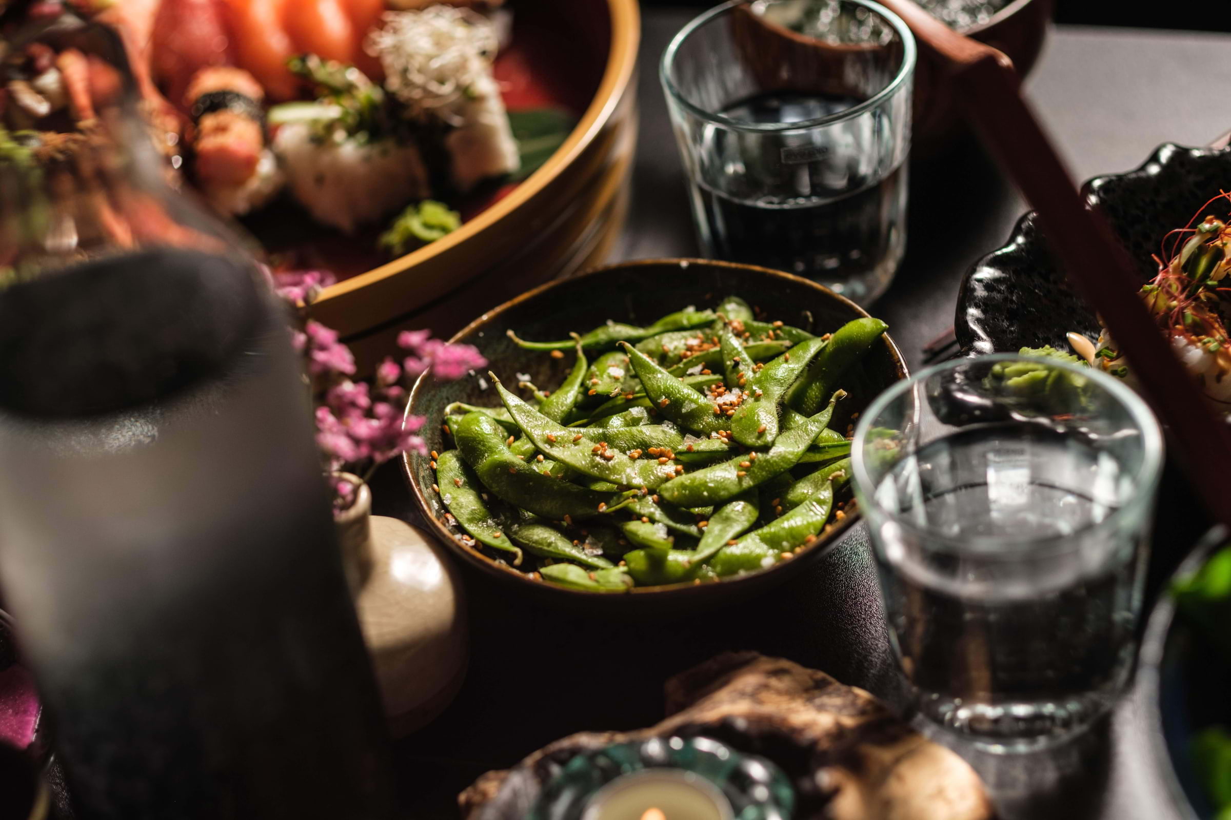 A bowl of edamame on a full table in a Japanese restaurant