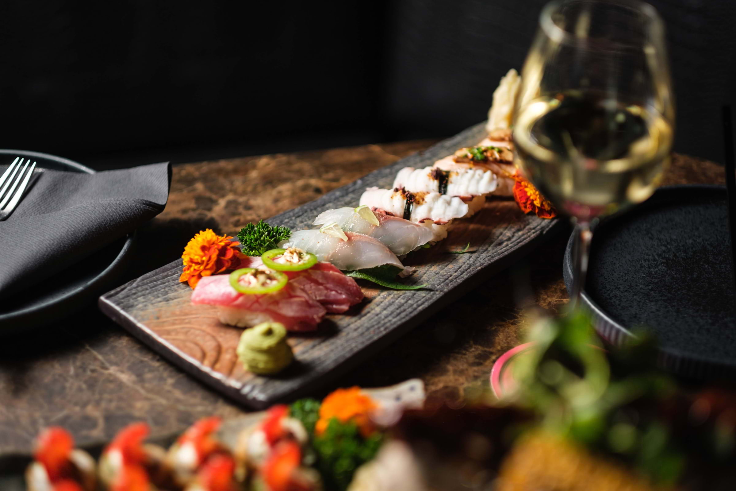 Several pieces of nigiri lined up on a black wooden board on a restaurant table