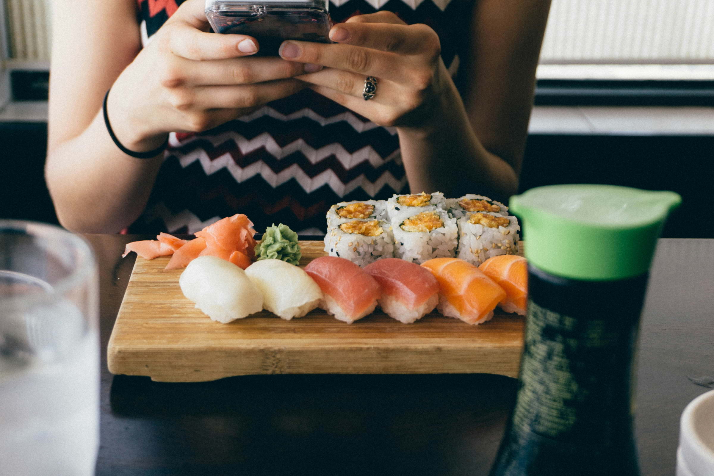 A woman taking a photo of sushi on a wooden board