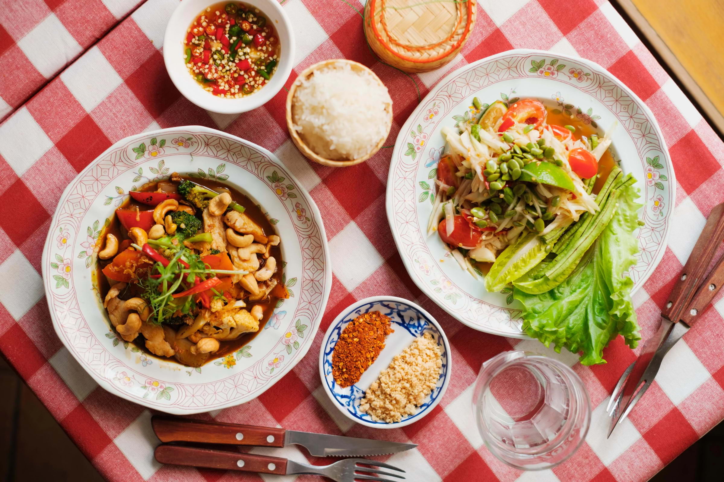 Thai dishes and condiments set out on a restaurant table with a red gingham tablecloth