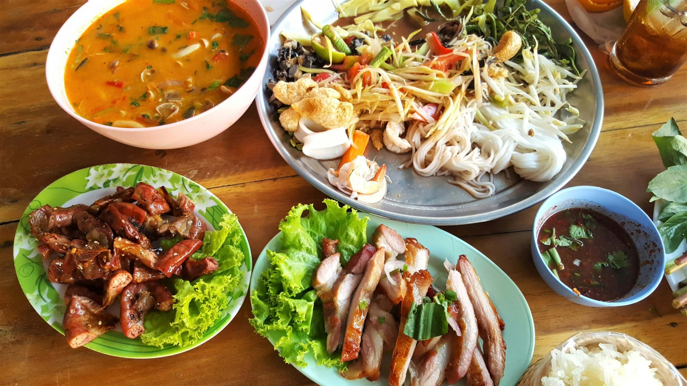 Four plates of colourful Thai food on a wooden table