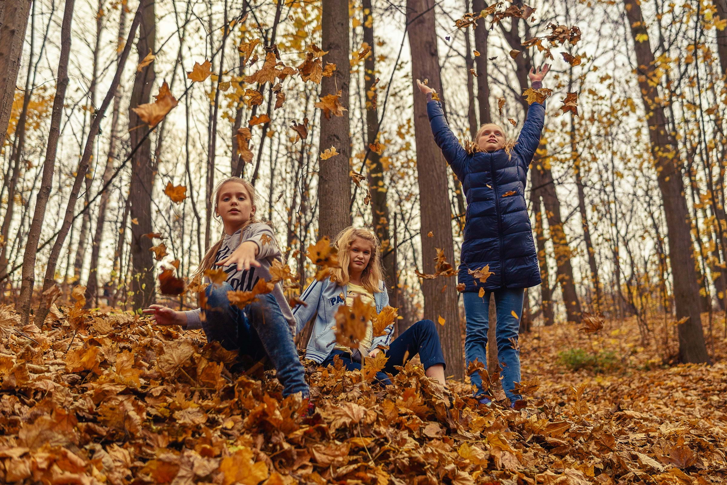 Three girls throwing autumn leaves in the park and having a good time