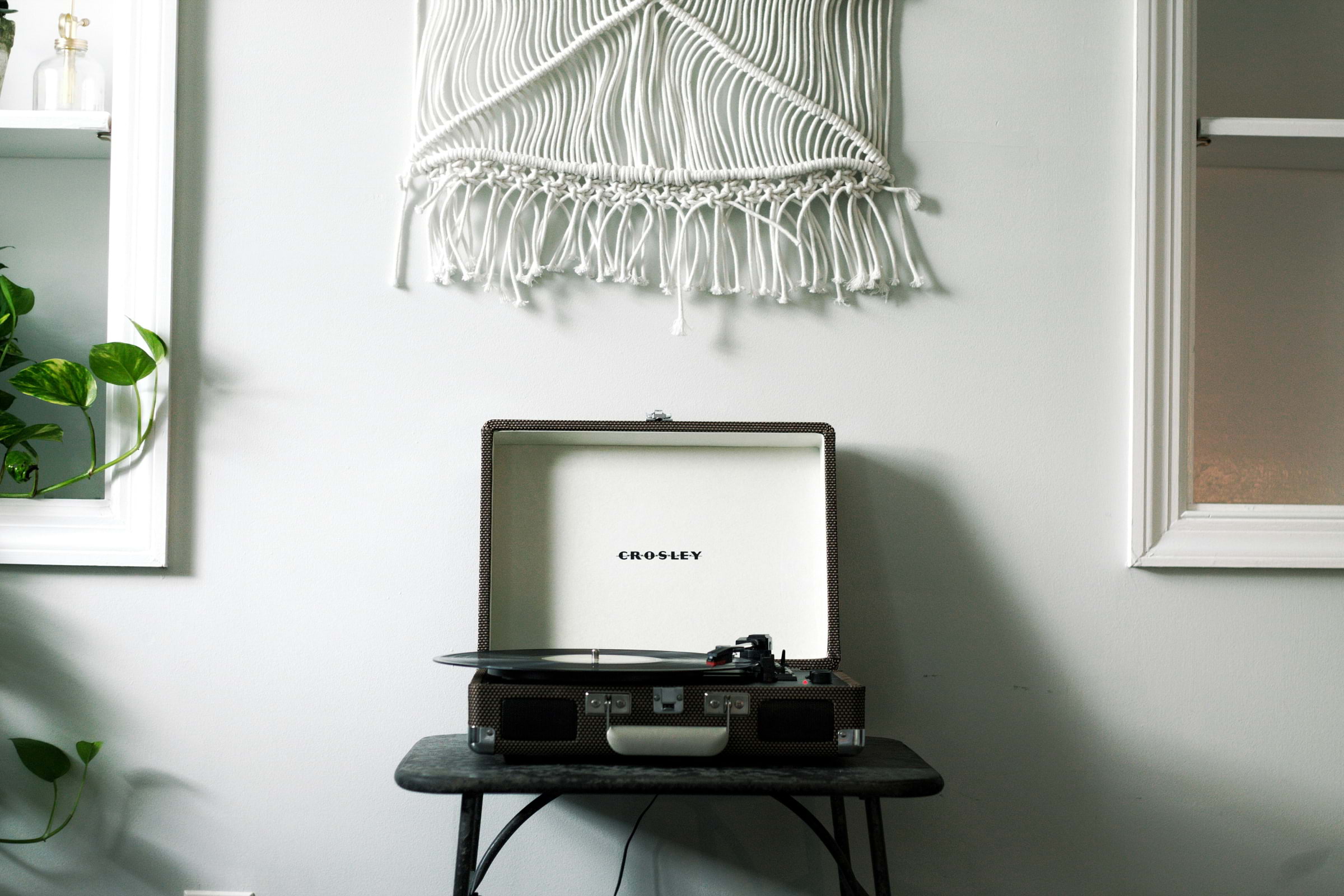 A record player with a hanging macrame wall piece above