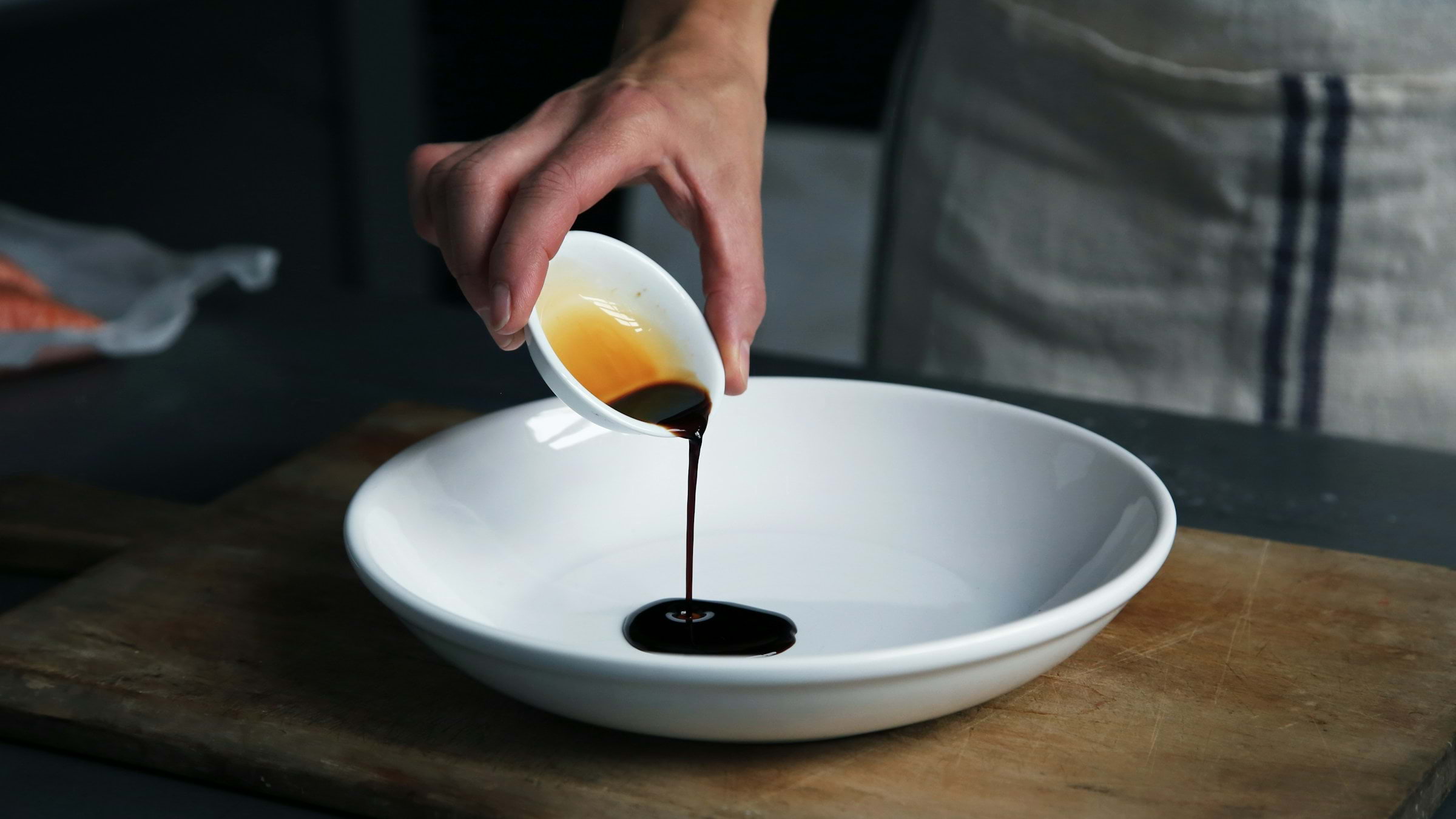 A chef dripping balsamic vinegar into a big white bowl