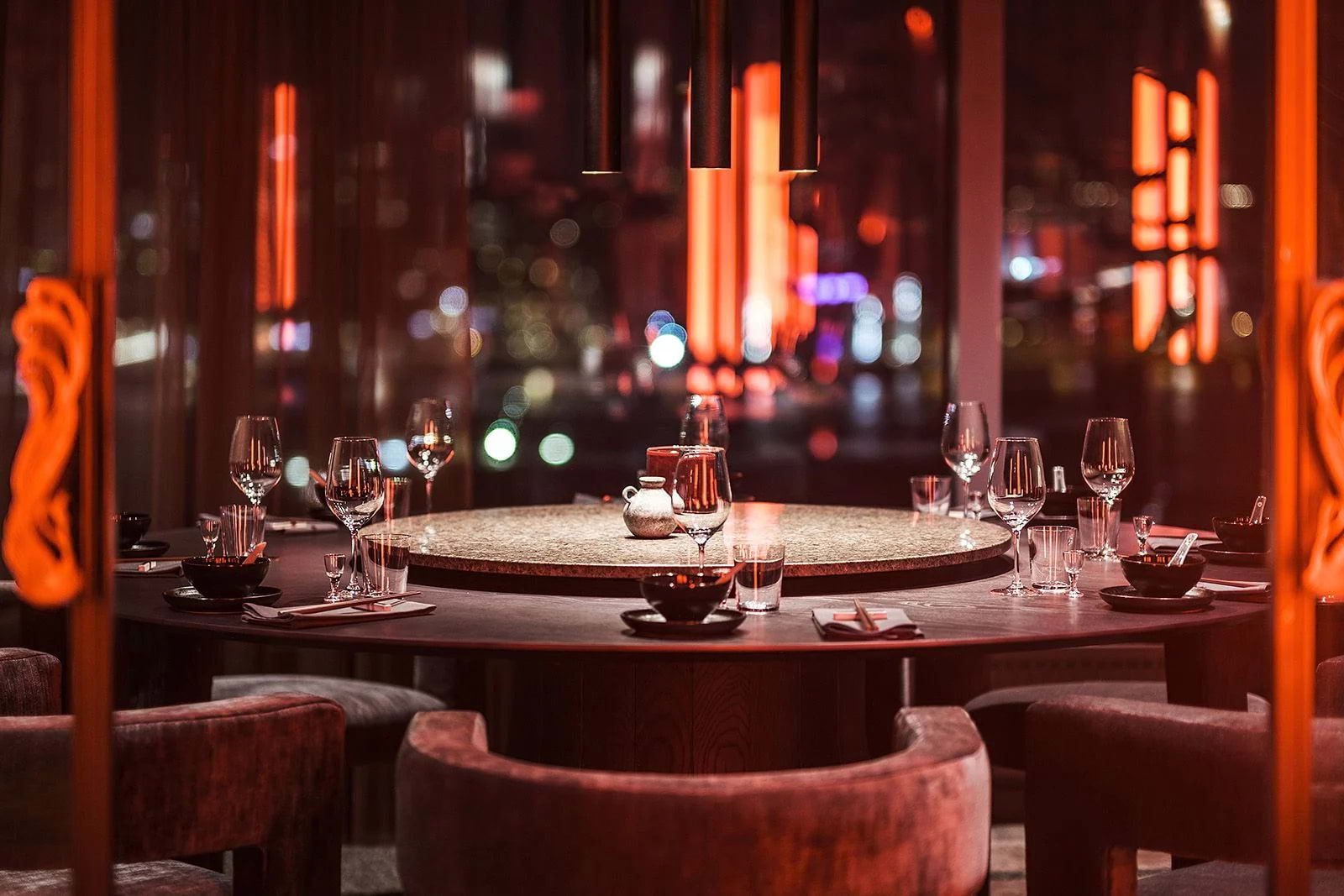 A night-time shot of a Lazy Susan with place settings in a Chinese restaurant with red lighting and big windows