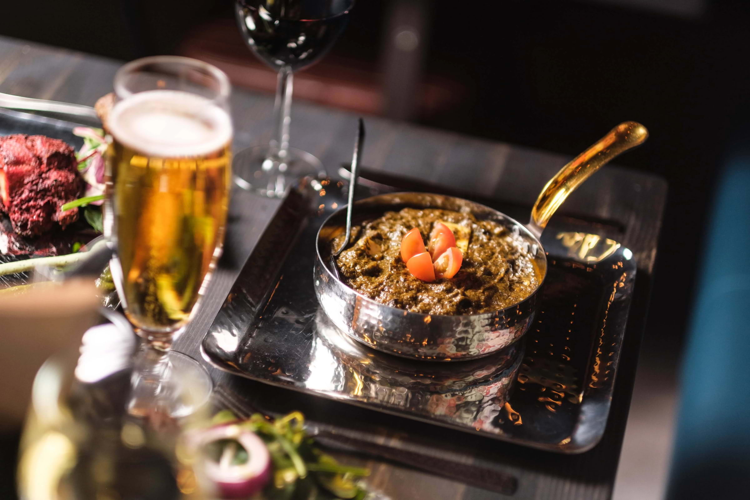 A curry served in a silver saucepan on a silver platter in a restaurant