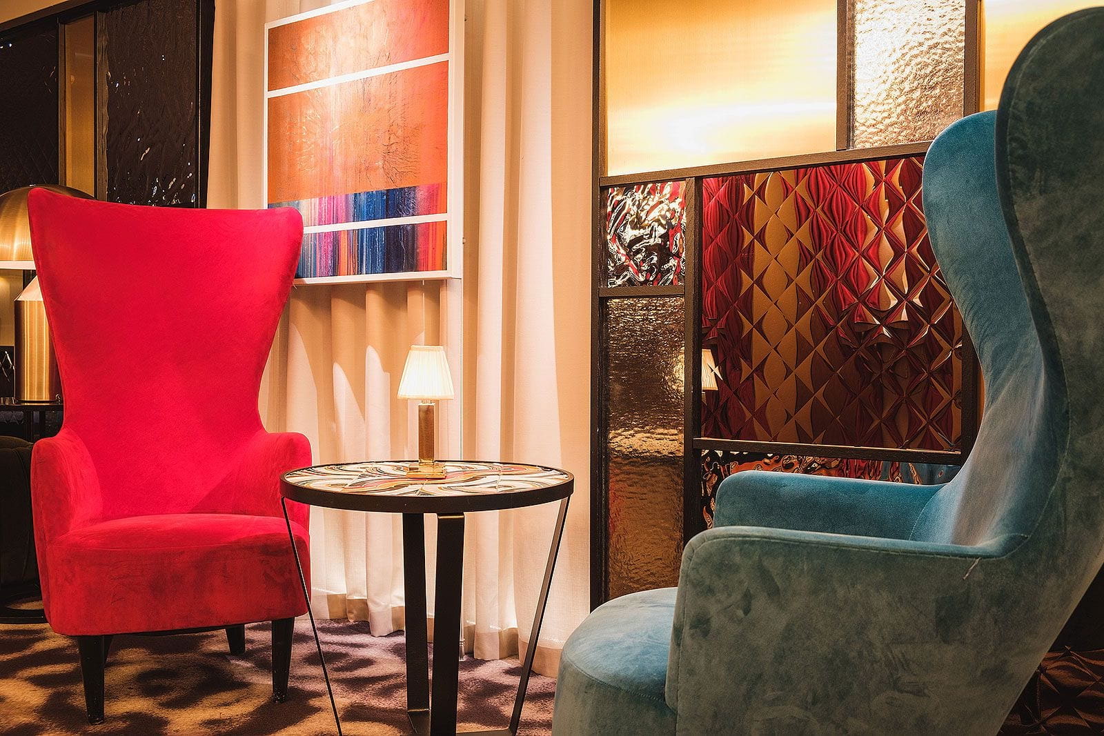 Two armchairs and a small round table with a lamp in a stylish, colourful hotel