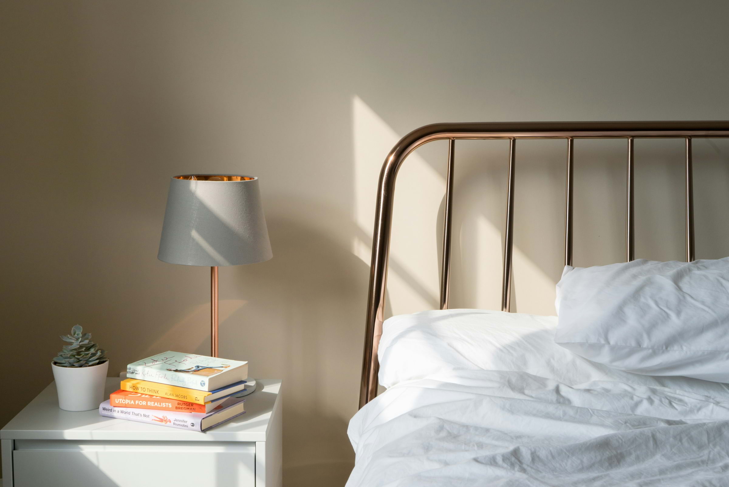 A metal bed with a white duvet and a bedside table with a lamp next to it