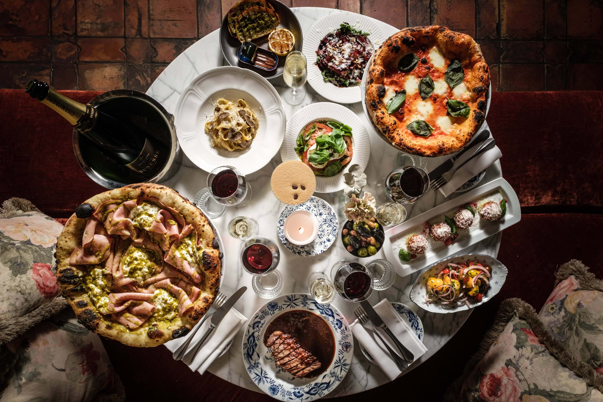 Pizzas, pasta, and other Italian dishes and drinks on a round restaurant table