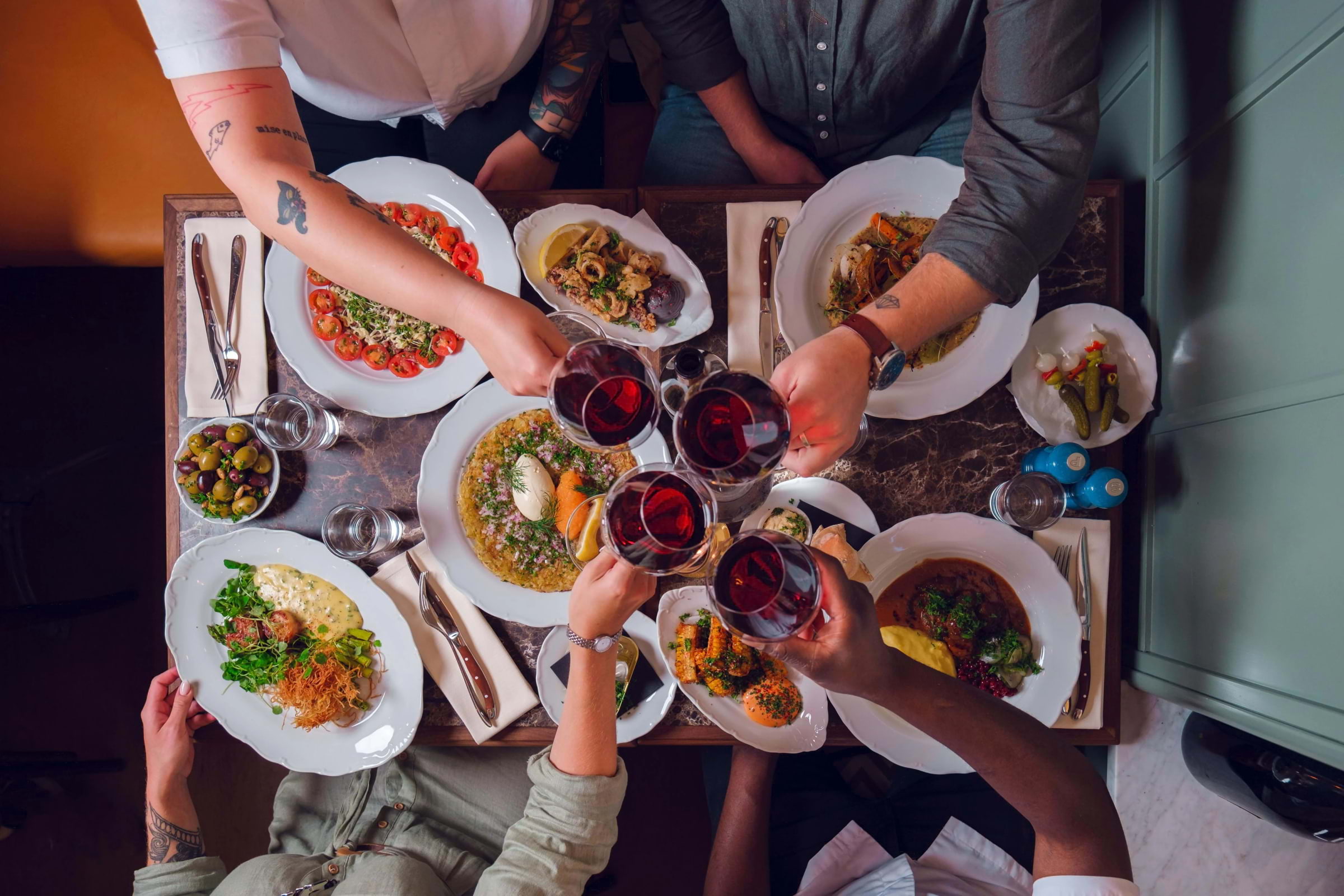 A group of people toasting red wine over a table covered in lunch dishes