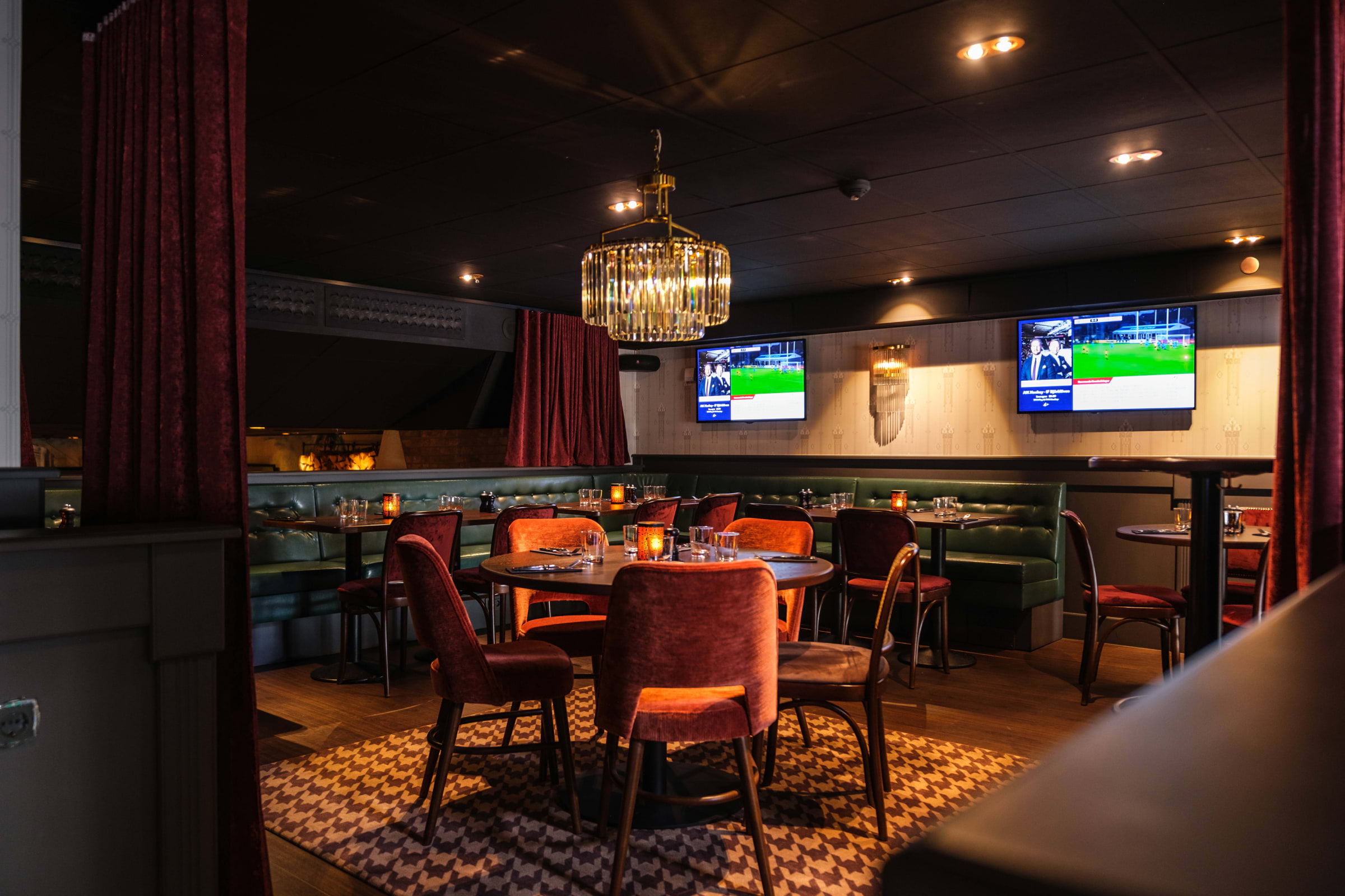 An elegant sports bar with tables, plush seating, and two TVs on the back wall