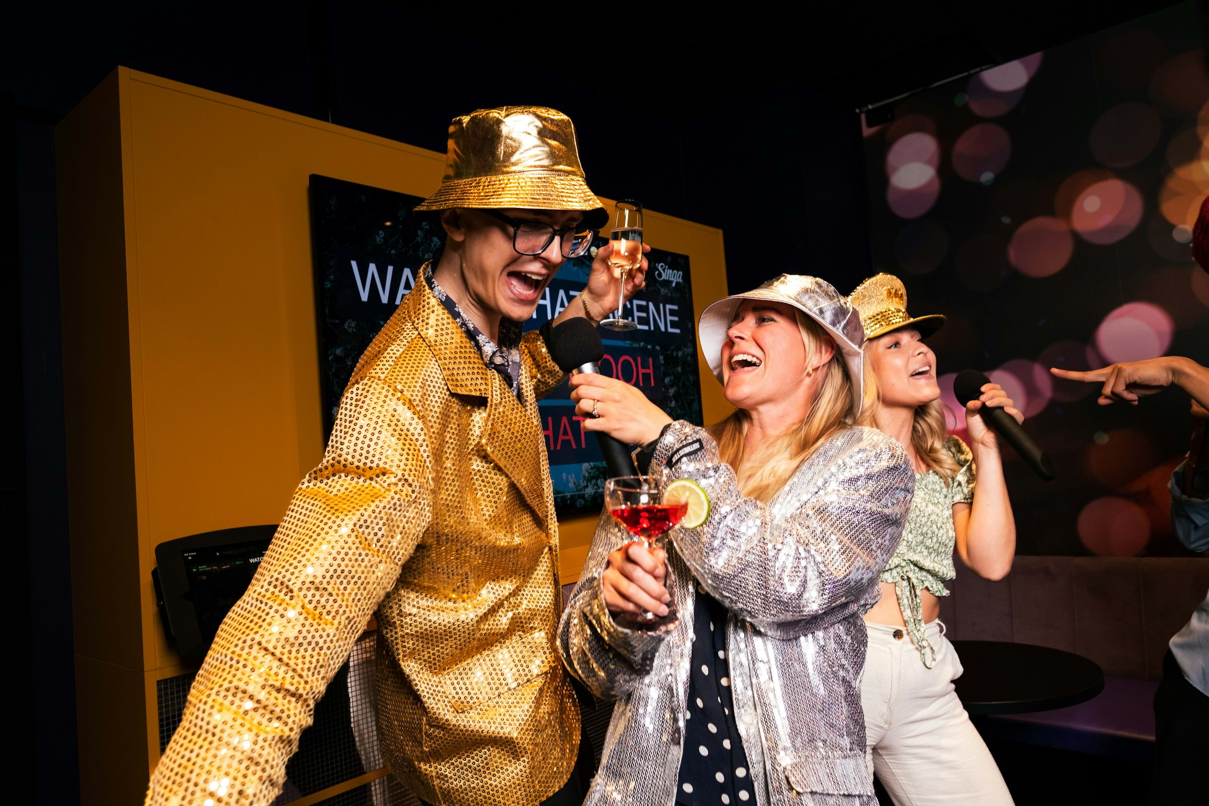 Three people in fancy dress singing karaoke in a bar