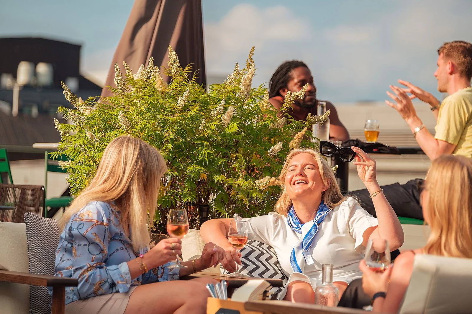 Three women with drinks laughing in the sun on a rooftop terrace