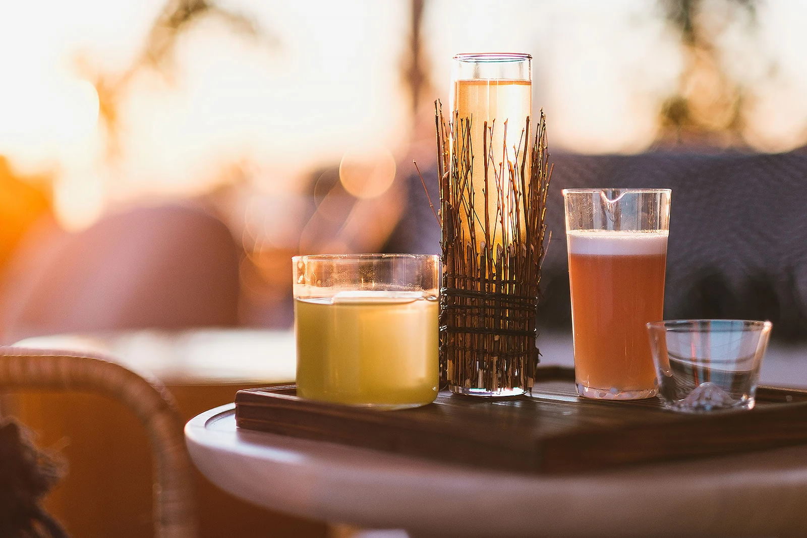 Three cocktails on a rooftop bar table at sunset