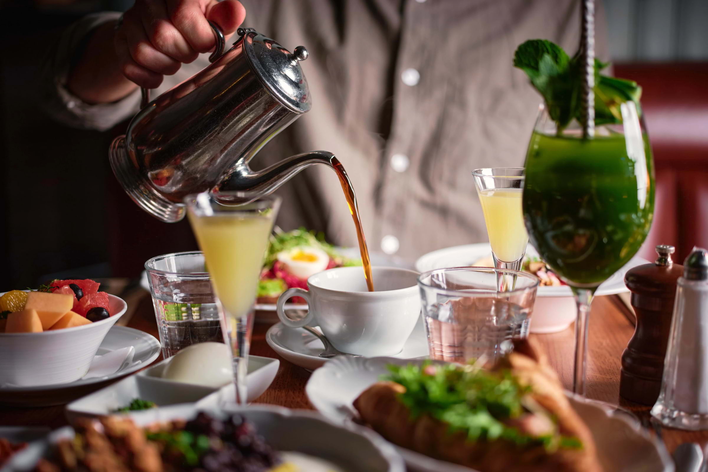A person pouring coffee into a cup on a table full of breakfast dishes