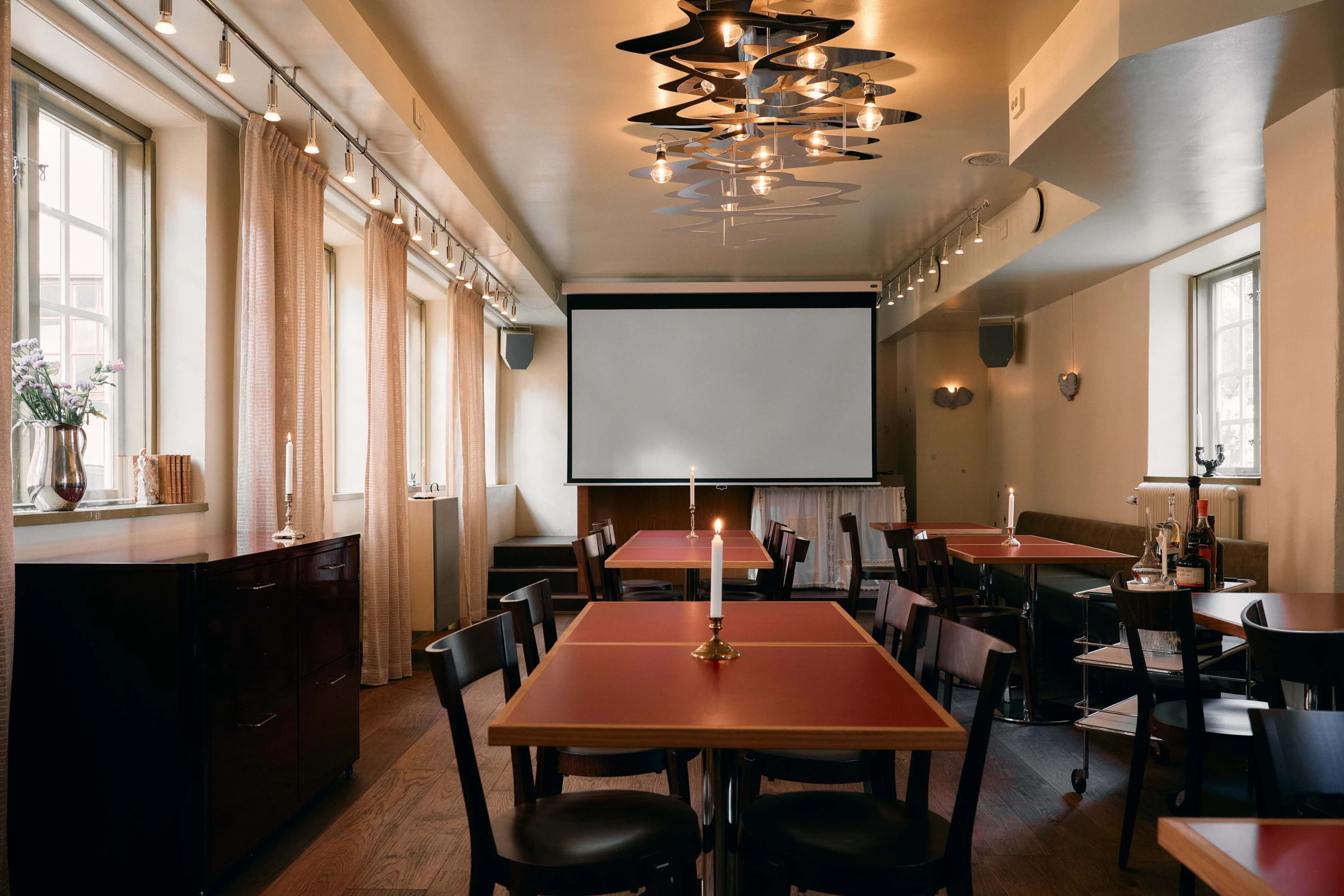 A private room with tables, lit candles, and a projection screen