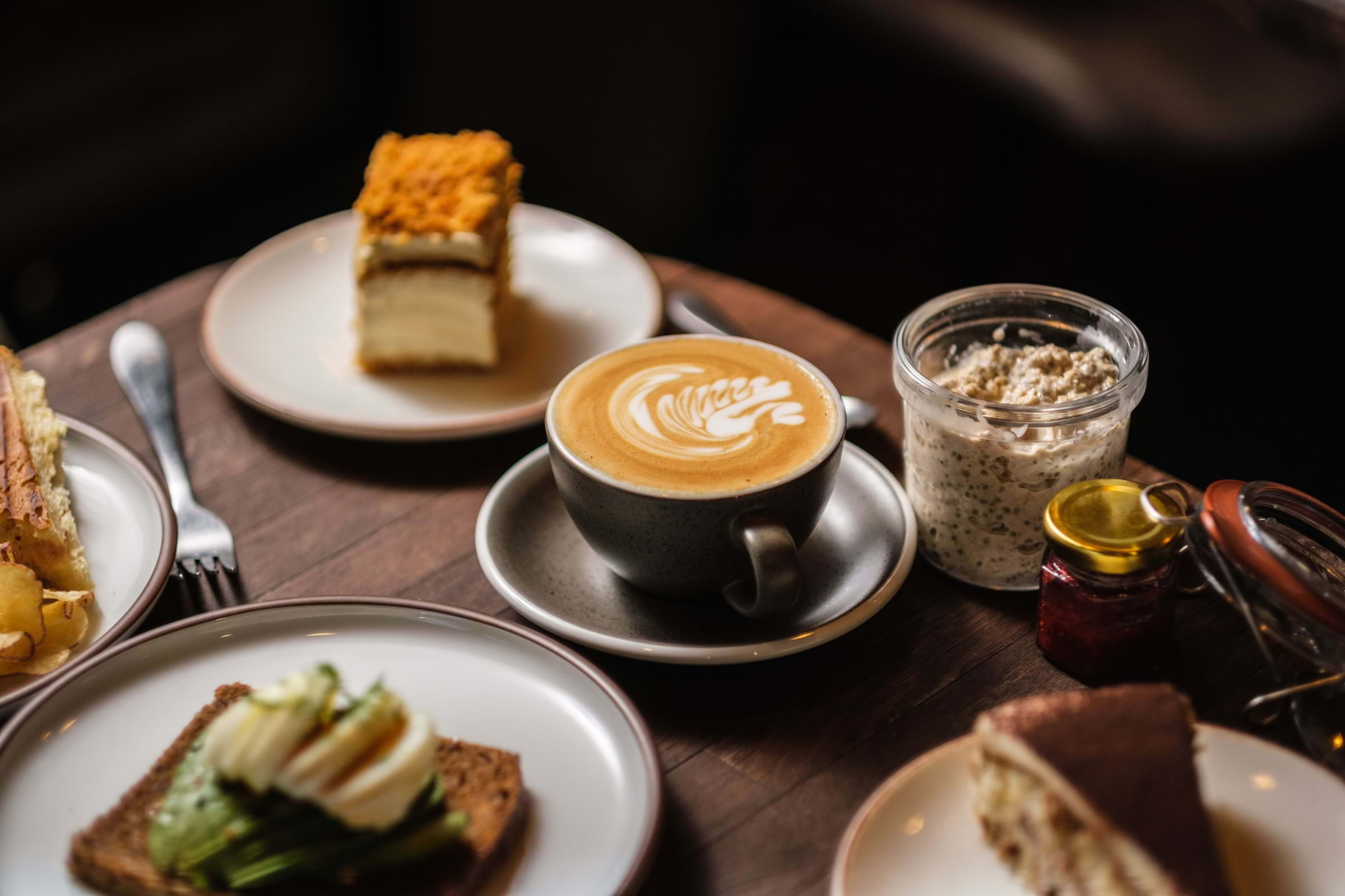 A latte in a black cup and other dishes on a wooden table in a caf&eacute;