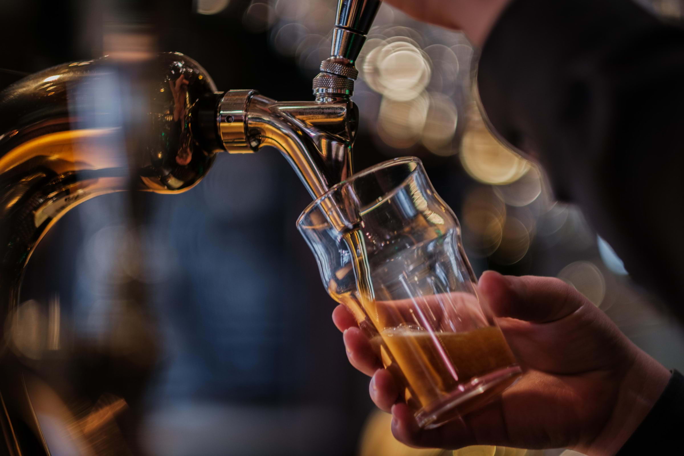 Close-up of a man pouring a pint from a gleaming beer tap