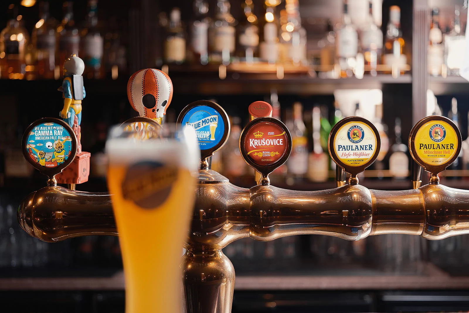 Close-up of a gleaming beer tap behind an out-of-focus pint